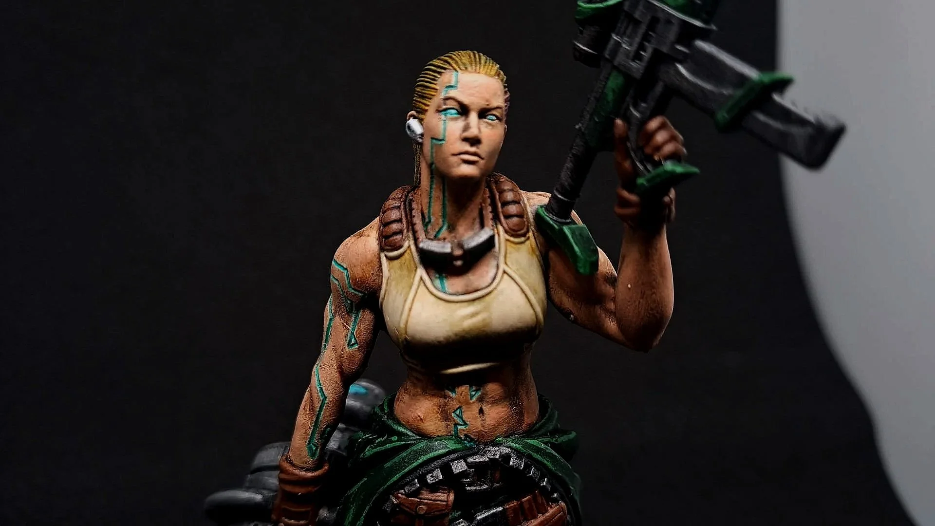 Detailansicht einer bemalten, kulturinspirierten Actionfigur einer weiblichen Kriegerin, die ein Gewehr trägt, mit Tattoos, braunem Oberkörper, grüner Hose und verschränkten Armen