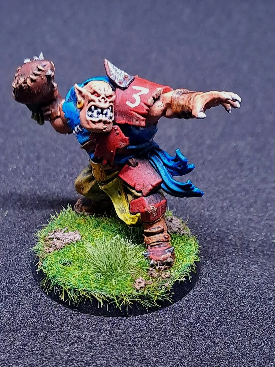 Eine detaillierte Miniatur-figur eines grimmig aussehenden Tuche Monster auf einem Grasgrundstück, das einen Baseballschläger schwingt.