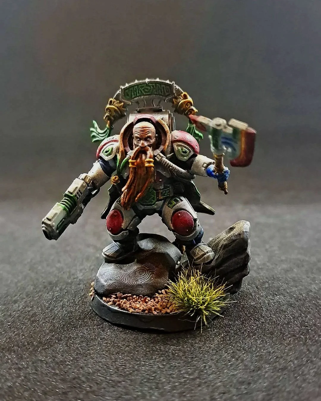 Kunstwerk eines bemalten Miniatur-Figurenkriegers in einem futuristischen Rüstung, mit Waffe in der Hand, auf einem Diorama-Untergrund mit Steinen und Pflanzen