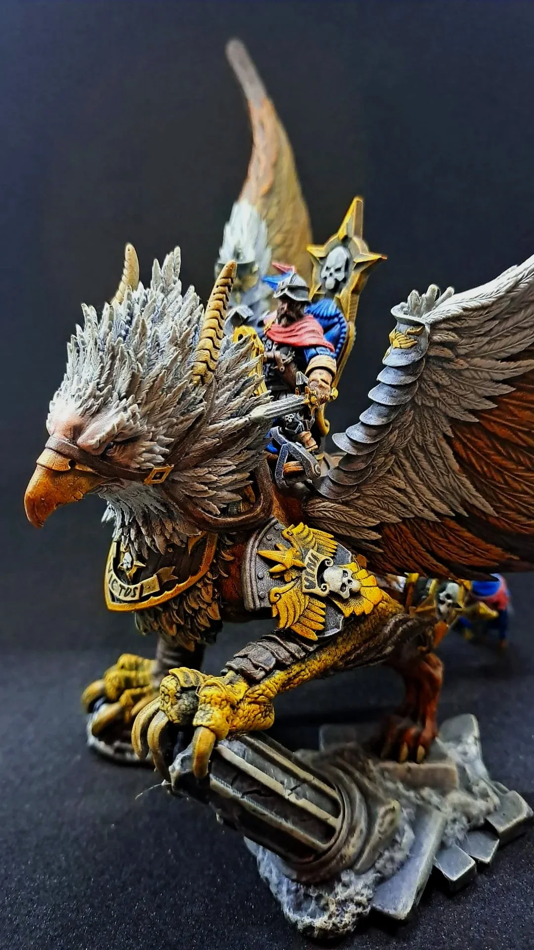 Ein detailliertes, farbig bemaltes Modell einer geflügelten Kriegsfigur, die auf einem großen Adler reitet, mit Rüstung und Schwertern auf dunklem Hintergrund.