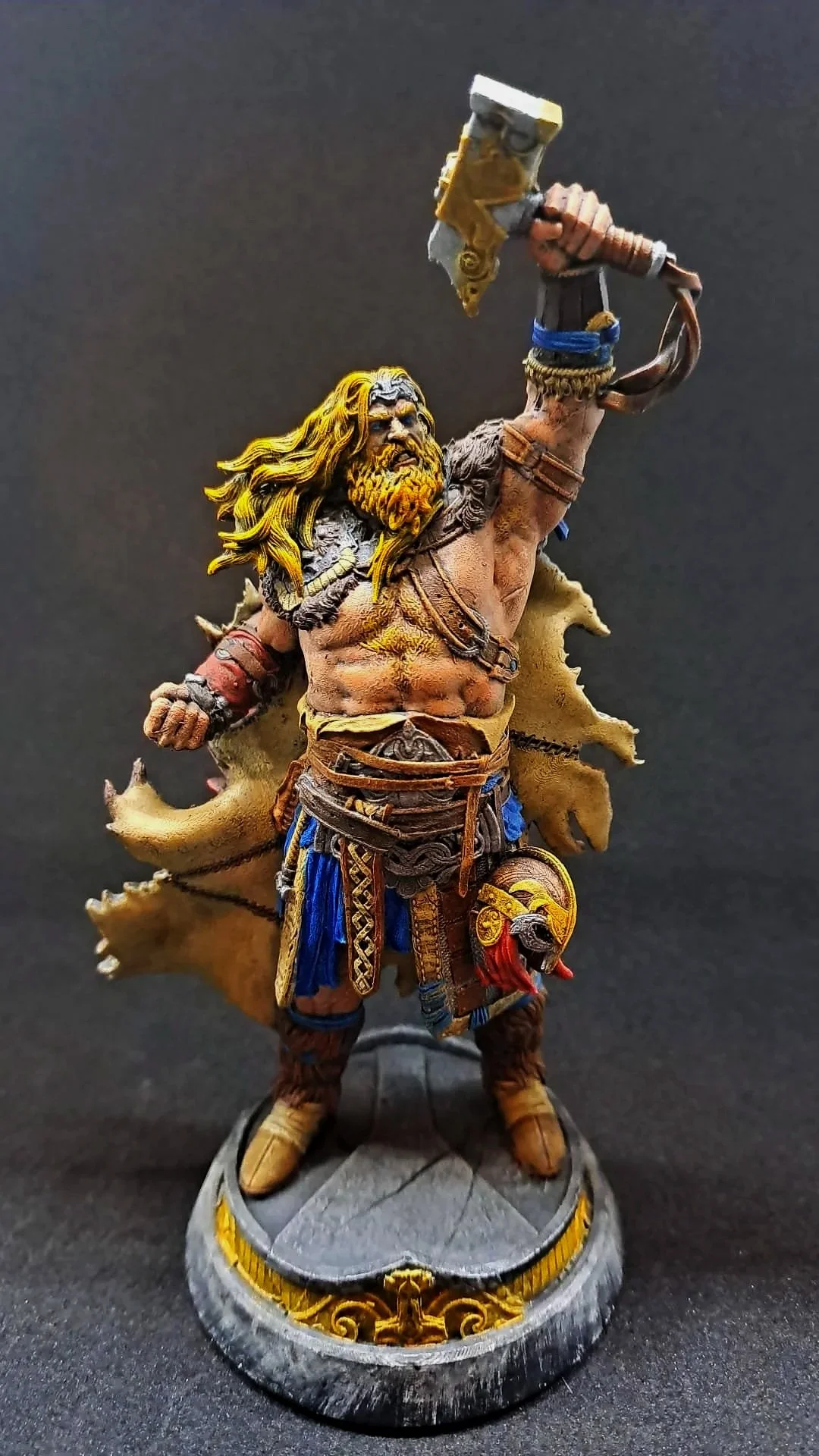 Eine detailreiche Fantasy-Figur eines Kriegers, der ein zerbrochenes Schwert in der erhobenen Hand hält, auf einem runden Sockel stehend, mit einem Löwenkopf-Motiv am Kleidungsstück.