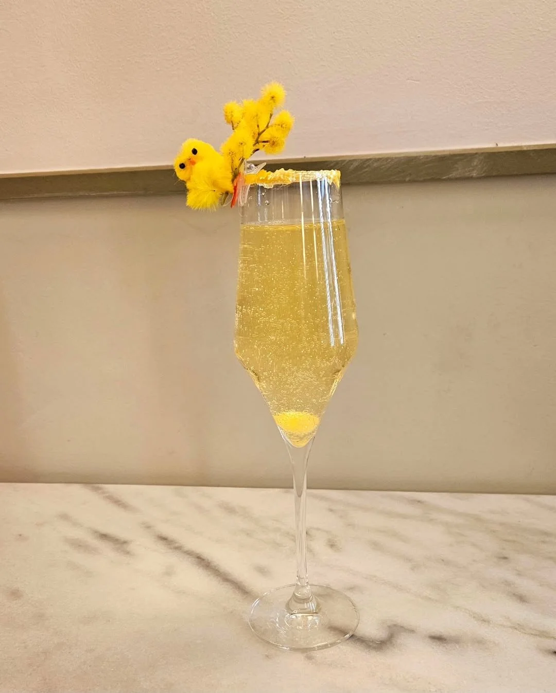 Verre à champagne avec décoration de brochette de fleurs et d'oiseaux en peluche jaune, garnie d'un bord de sucre en forme de cercle.