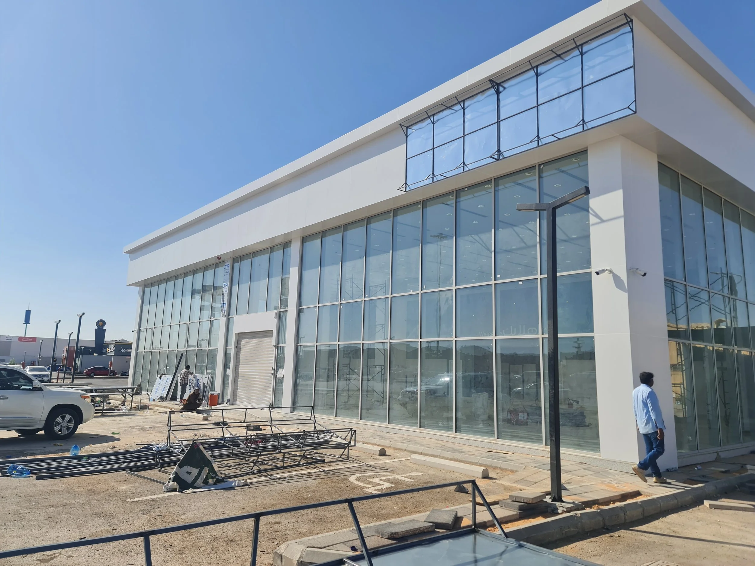 Under construction modern glass building in a parking lot with construction workers and equipment.