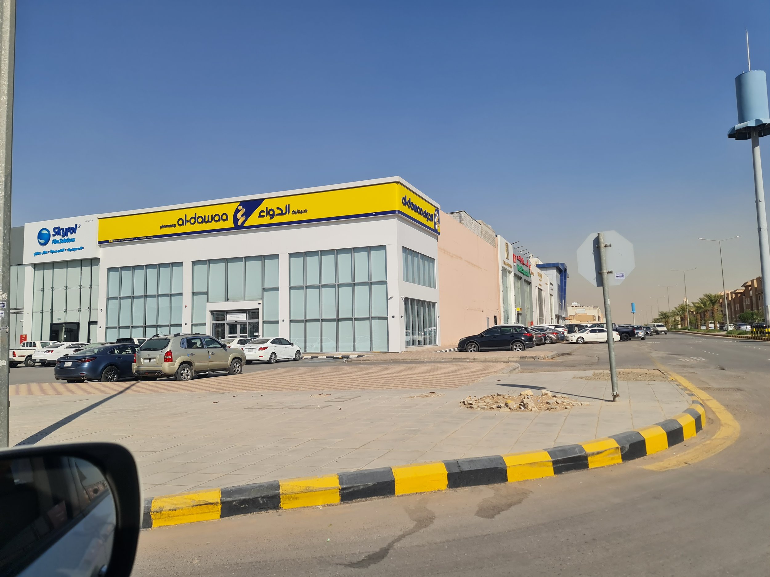 Commercial building with yellow and blue signage, parked cars in front, sidewalk, stop sign, and palm trees on the street, shot on a clear day.