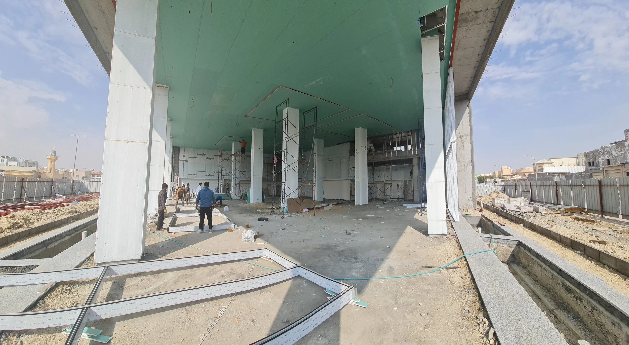 Construction site with workers, scaffolding, and partially built structure, including pillars and a green ceiling.