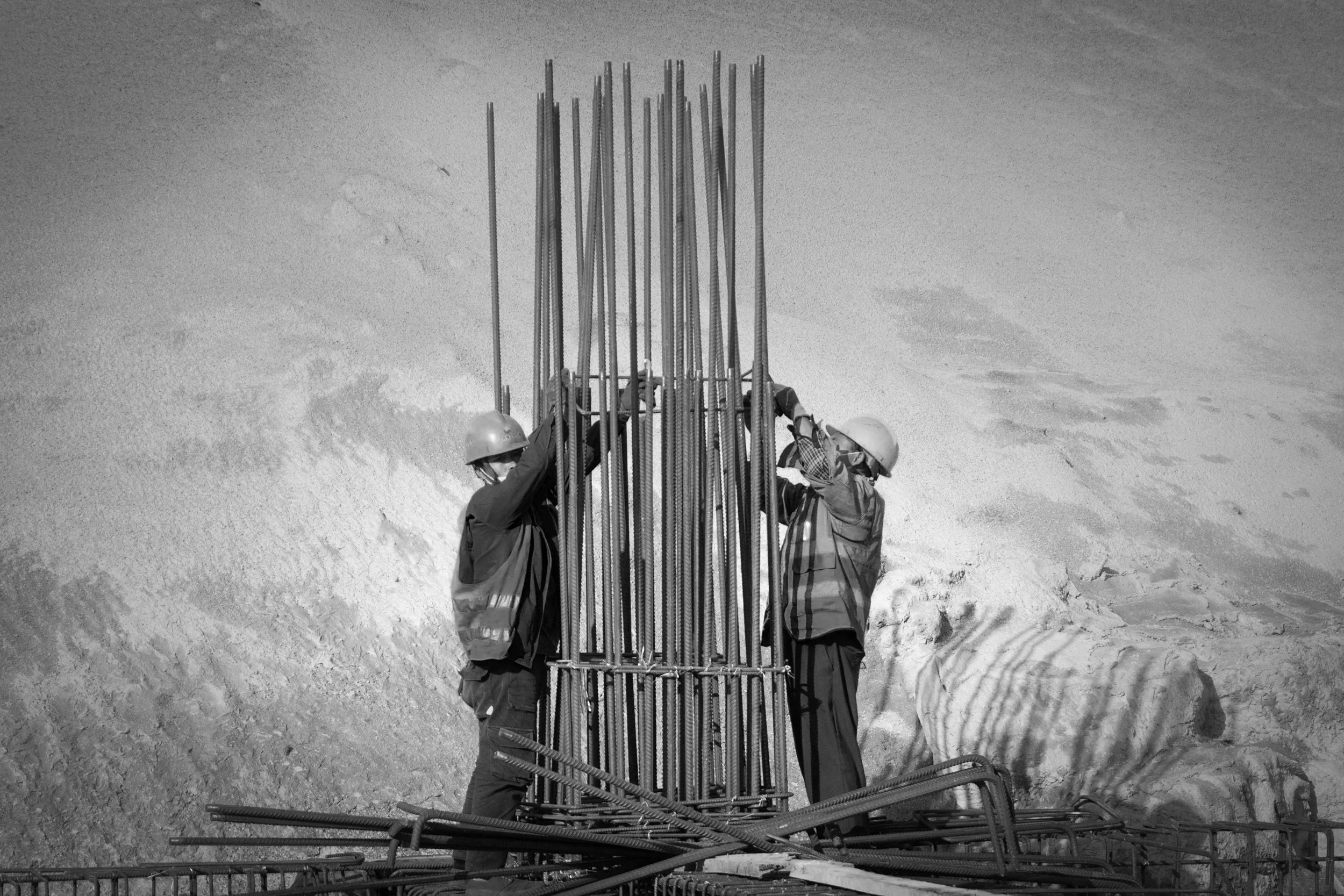 Two construction workers in helmets working with rebar on a construction site.