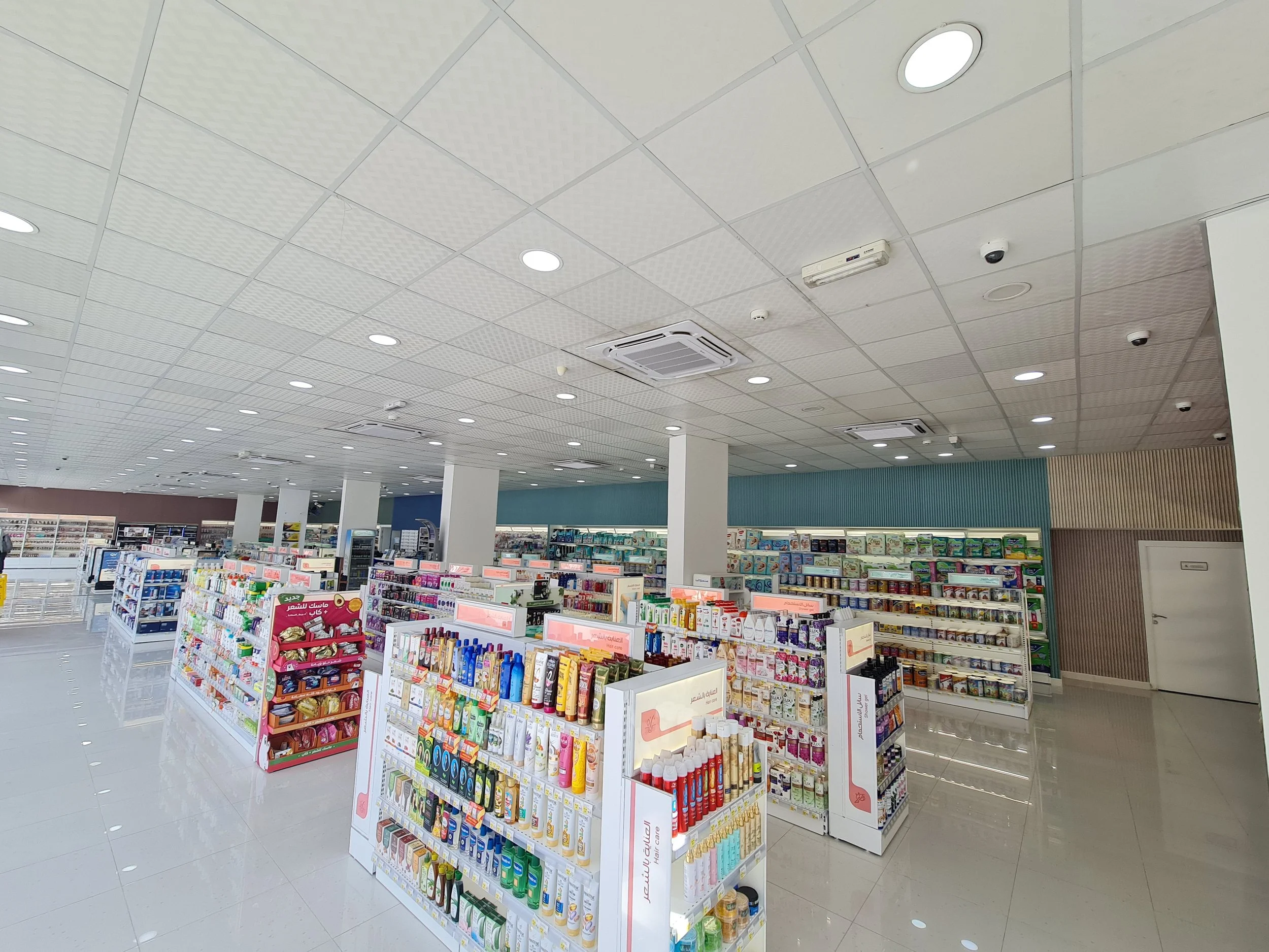 Interior of a modern pharmacy or drugstore with multiple shelves filled with various health and beauty products, brightly lit with ceiling lights.