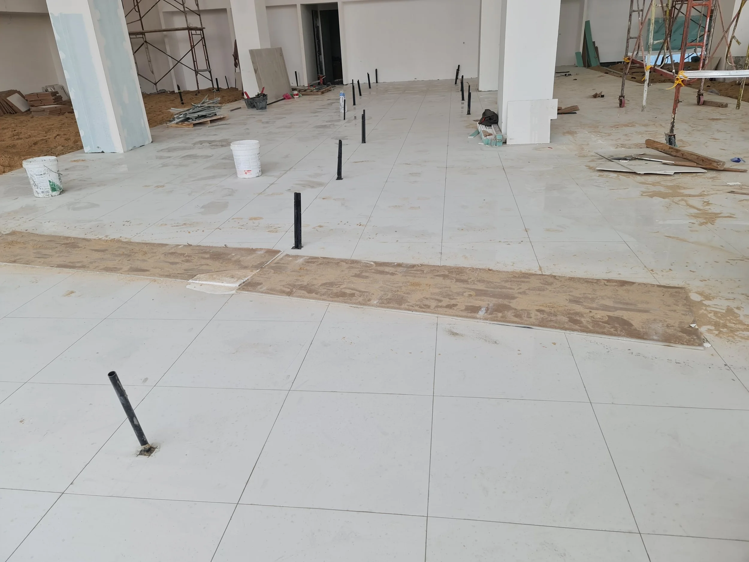 Construction site with tiled floor, scaffolding, buckets, and tools, in the process of building or renovating interior space.