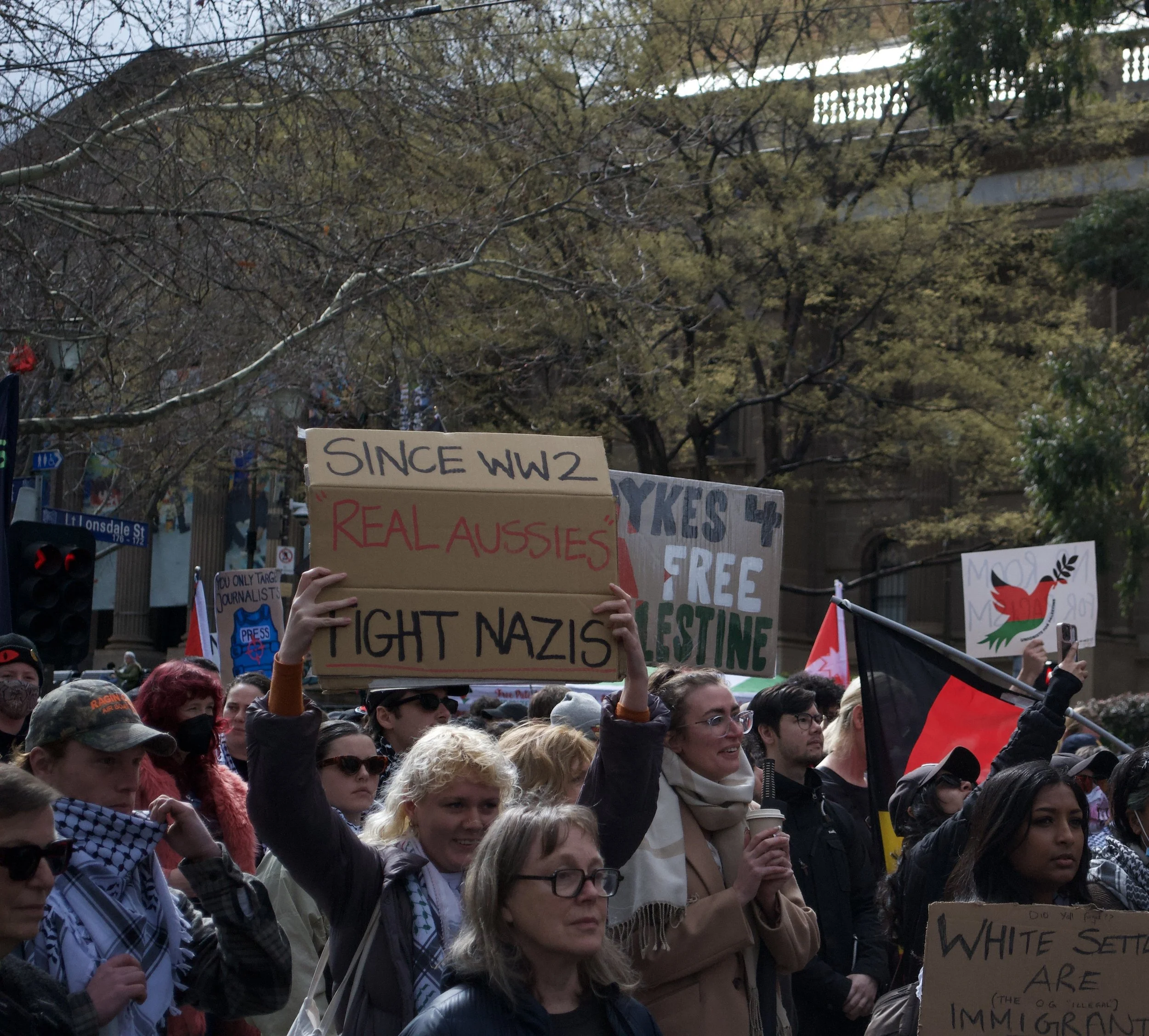 A counter protester holds up a sign 'Since WW2 REAL AUSSIES Fight Nazis' in front of State Library on Swanston Street.