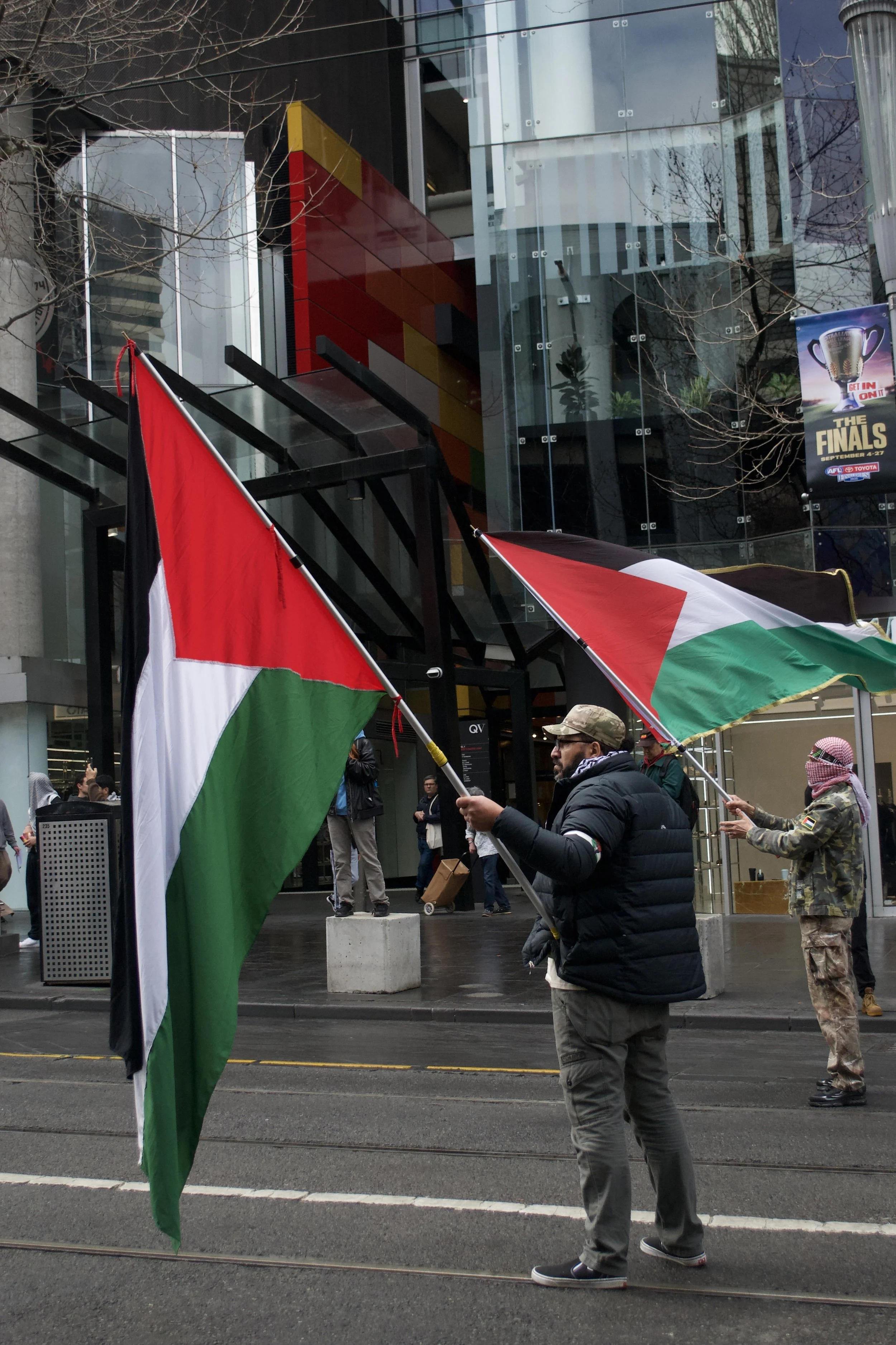 Two counter protesters wave the Palestinian Flag out the front of QV on Swanston Street.