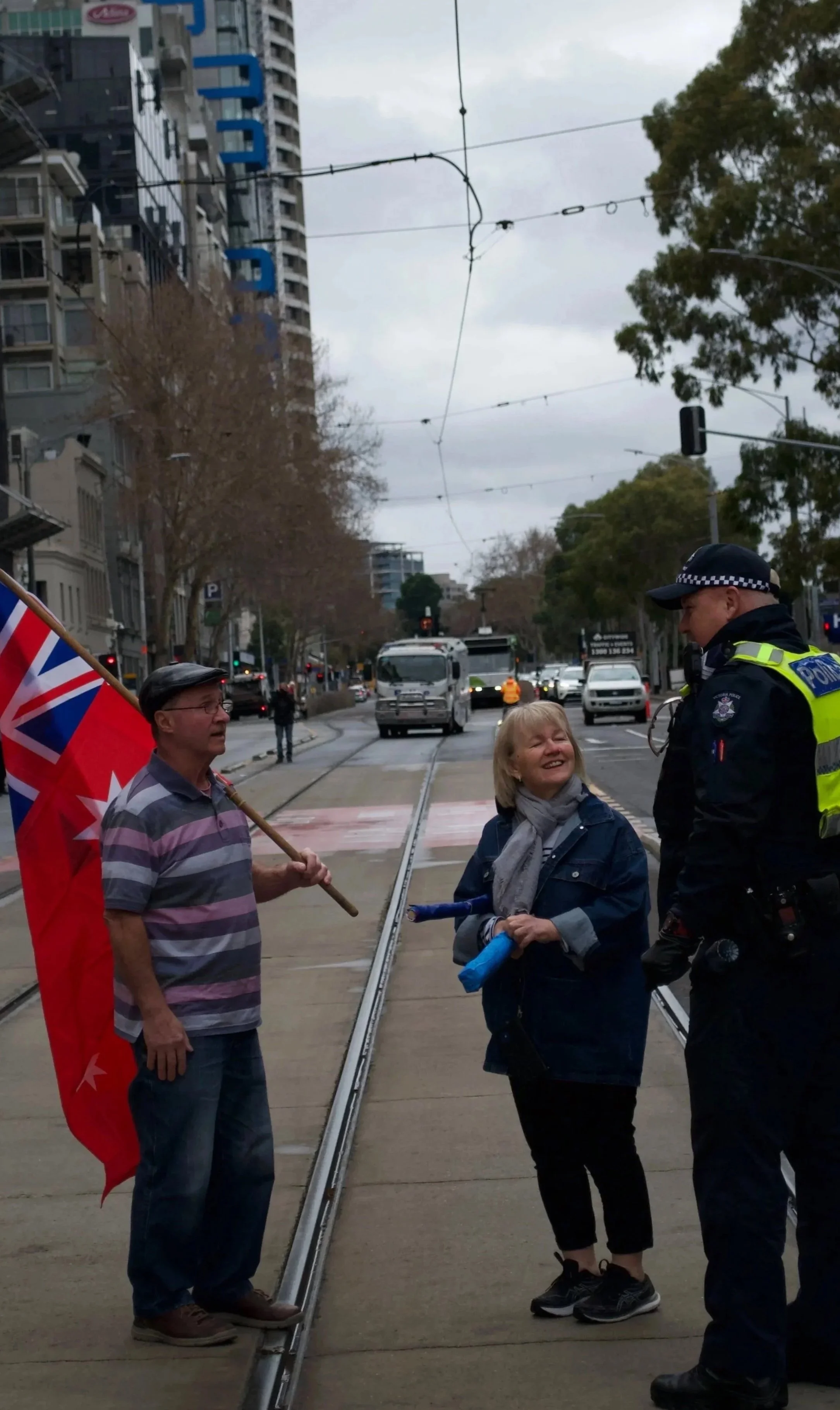 A Victoria Police Officer speaks with 'March for Australia' protesters one of which is carrying the Red Ensign flag on Flinders Street.