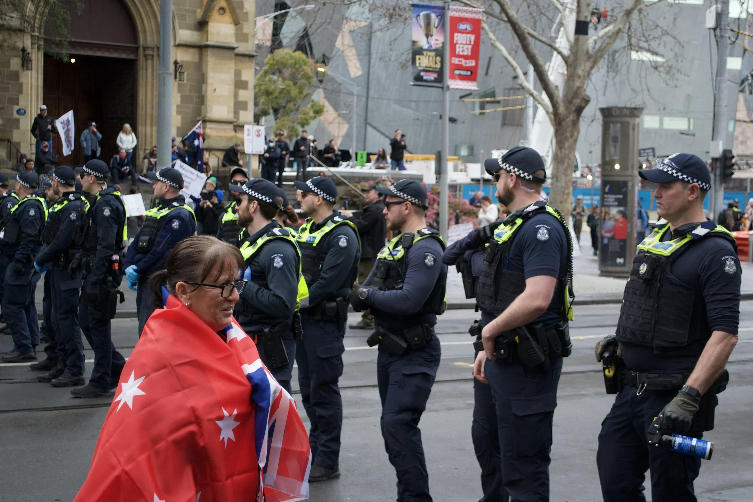 A woman draped in the Red Ensign flag walks past a police line separating 'March for Australia' protesters and the counter protest at the corner of Swanston Street and Flinders Street.