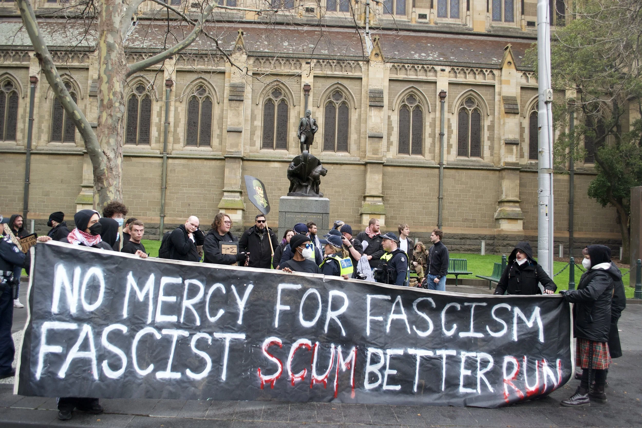 Counter protesters hold up a banner 'No Mercy For Fascism Fascist Scum Better Run' next to St Paul's Cathedral on Swanston Street.