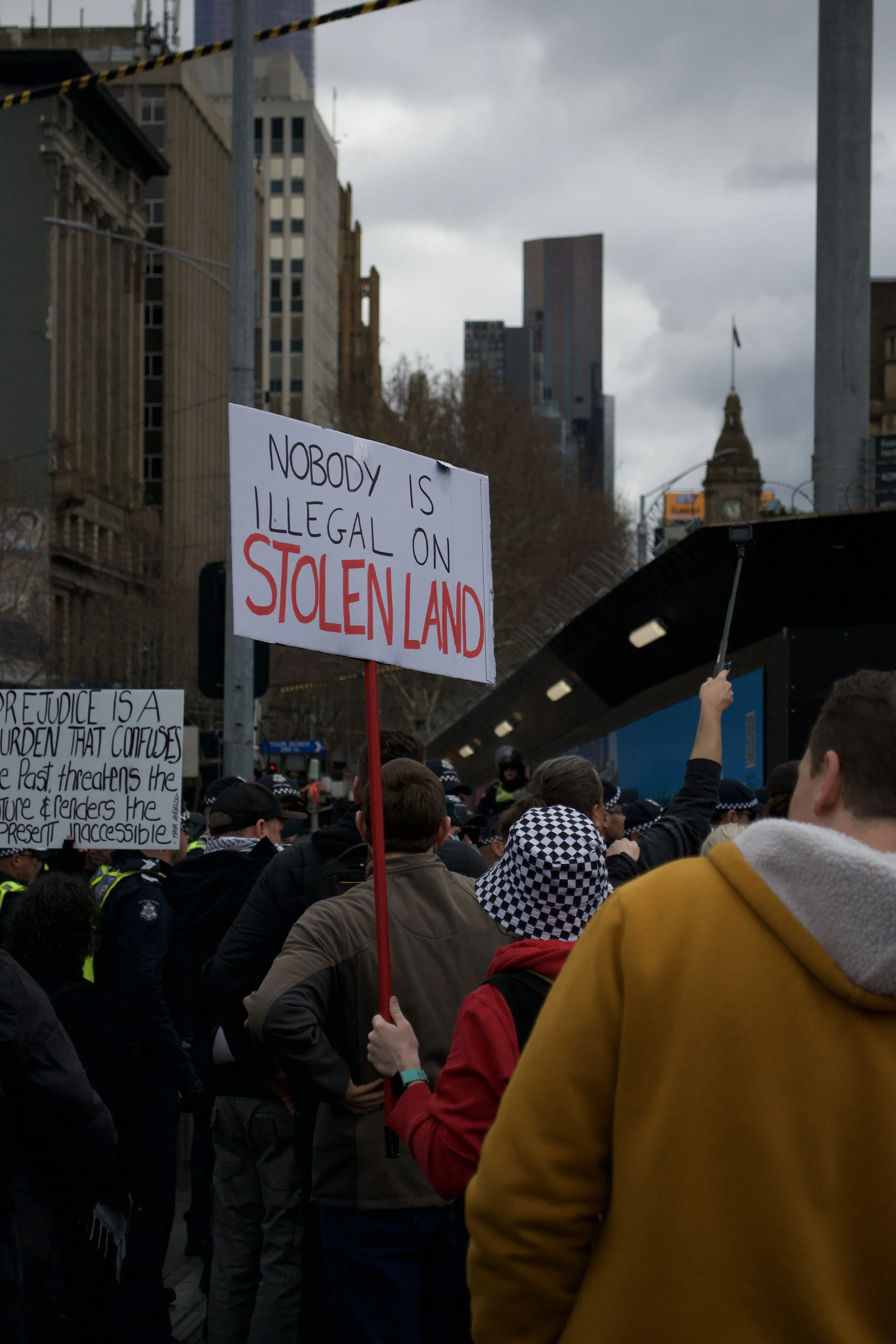A counter protester holds up a sign 'Nobody Is Illegal On STOLEN LAND' at Fed Square