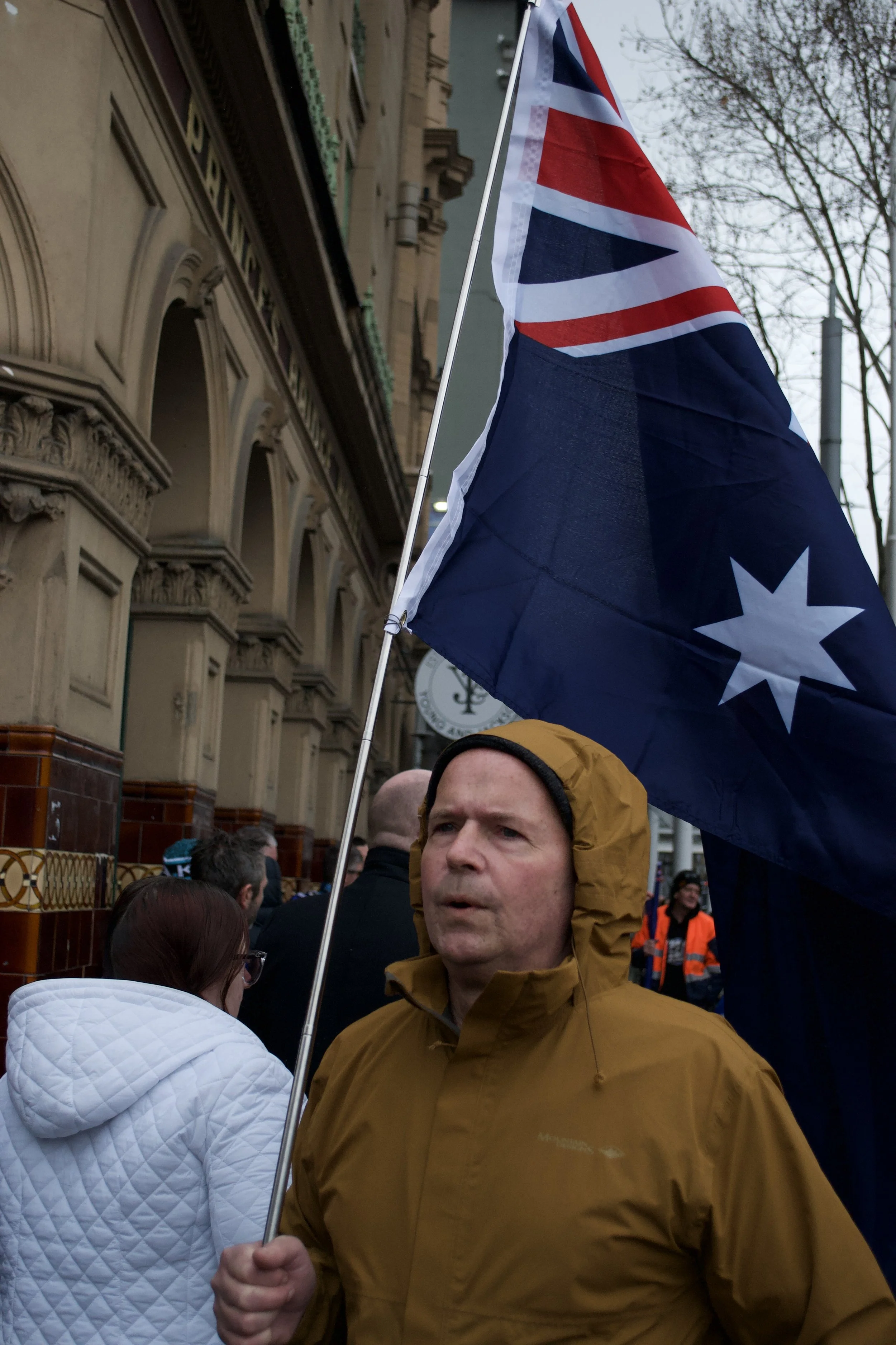 A man carrying the Australian flag walks toward the 'March for Australia' protest on the corner of Flinders Street and Swanston Street.