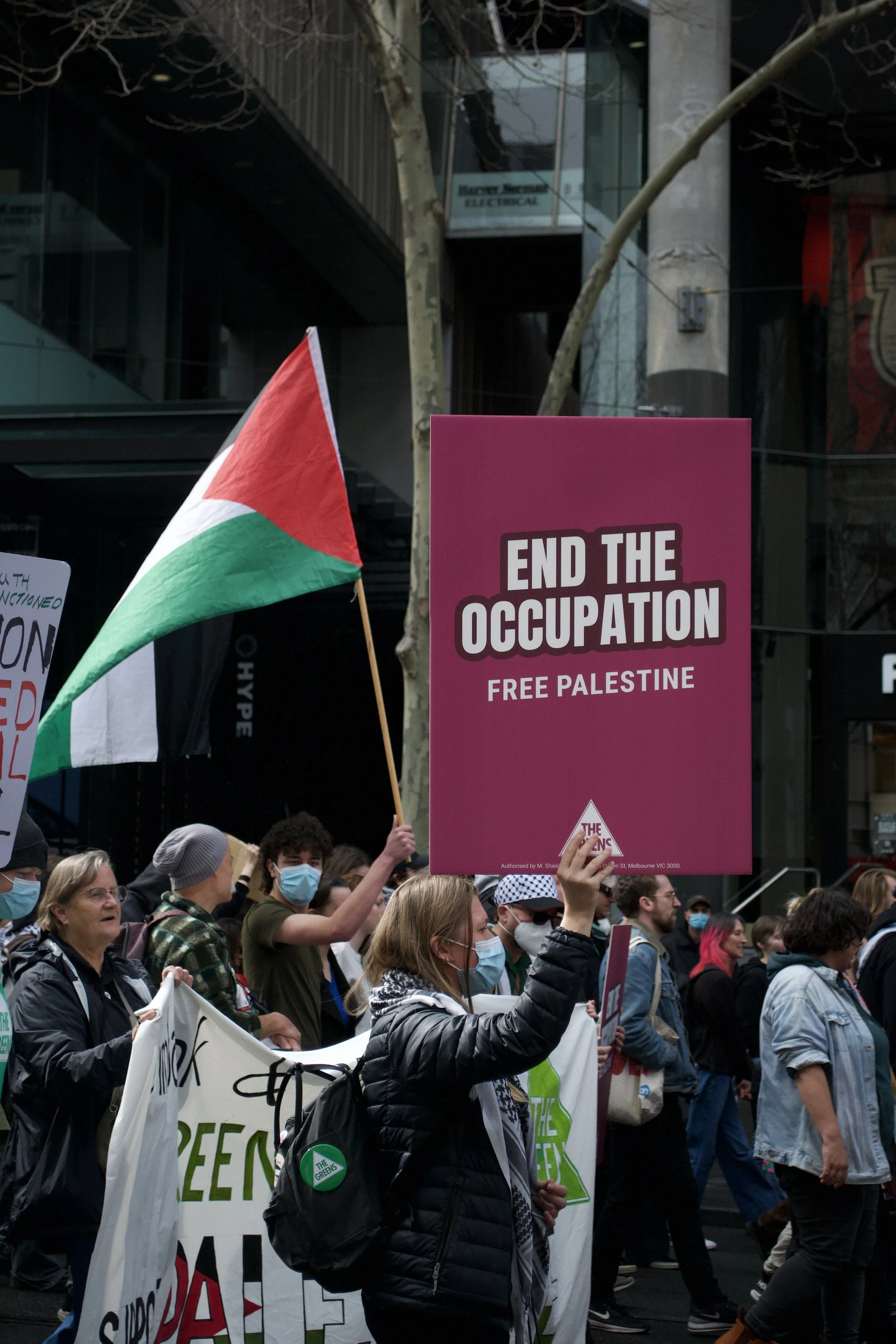 A counter protester holds up a Greens Party sign 'End The Occupation Free Palestine' on the corner of Swanston Street and Little Lonsdale Street.