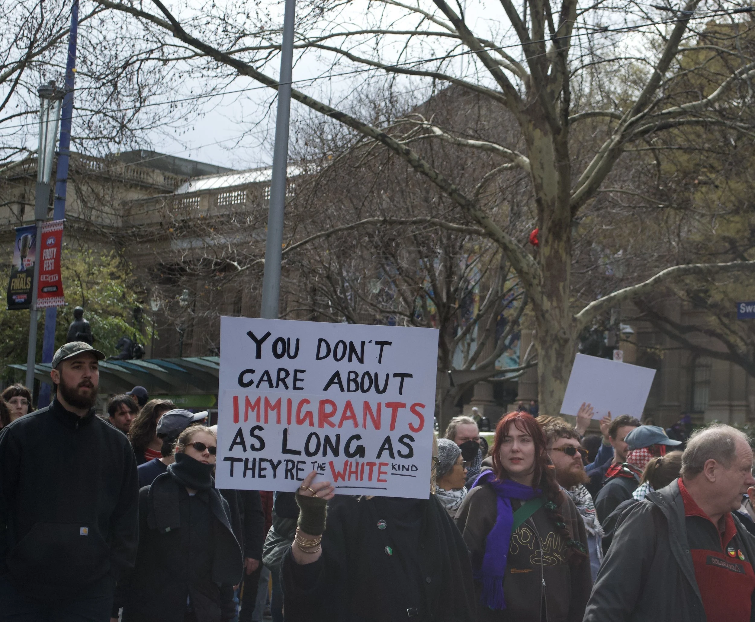A counter protester holds up a sign 'You Don't Care About IMMIGRANTS As Long As They're The WHITE Kind' in front of State Library on Swanston Street.