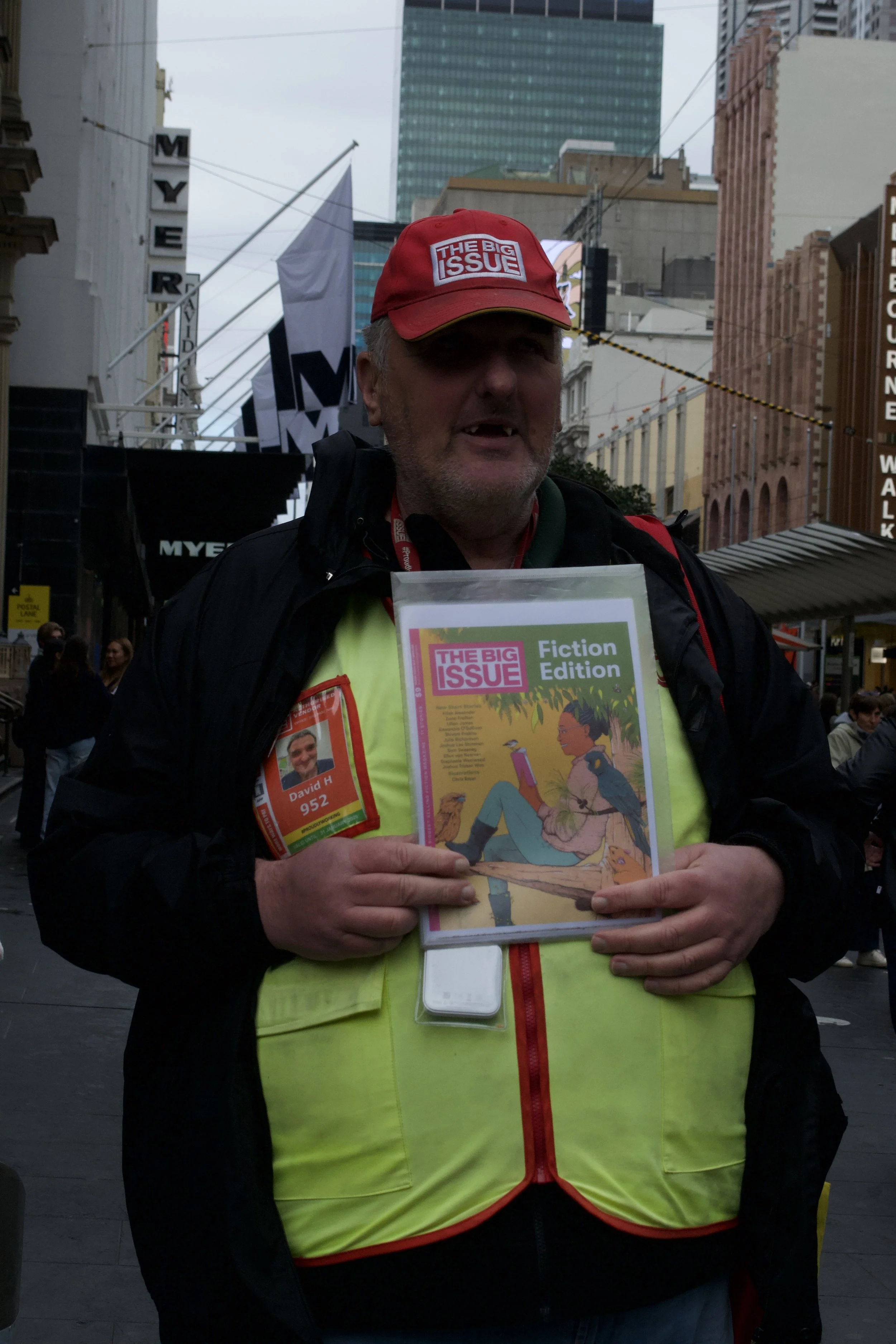 A man selling 'The Big Issue' magazine, a company "dedicated to supporting and creating work opportunities for people experiencing homelessness, marginalisation and disadvantage" as per their website on Bourke Street (30.08.2025)