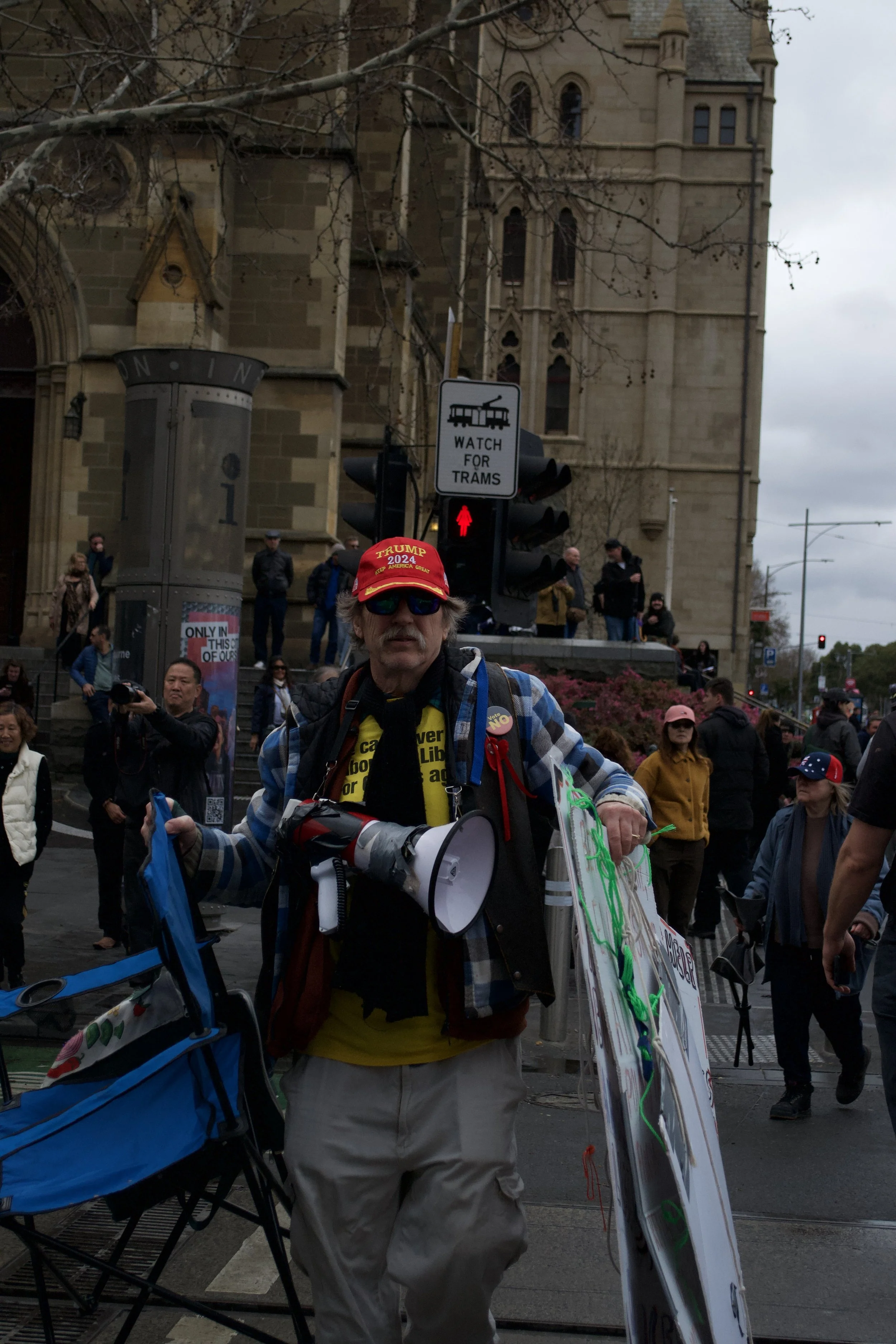 A man wearing a 'Trump 2024' hat and a 'Vote No' pin walks towards the 'March for Australia' protest in front of St Paul's Cathedral.