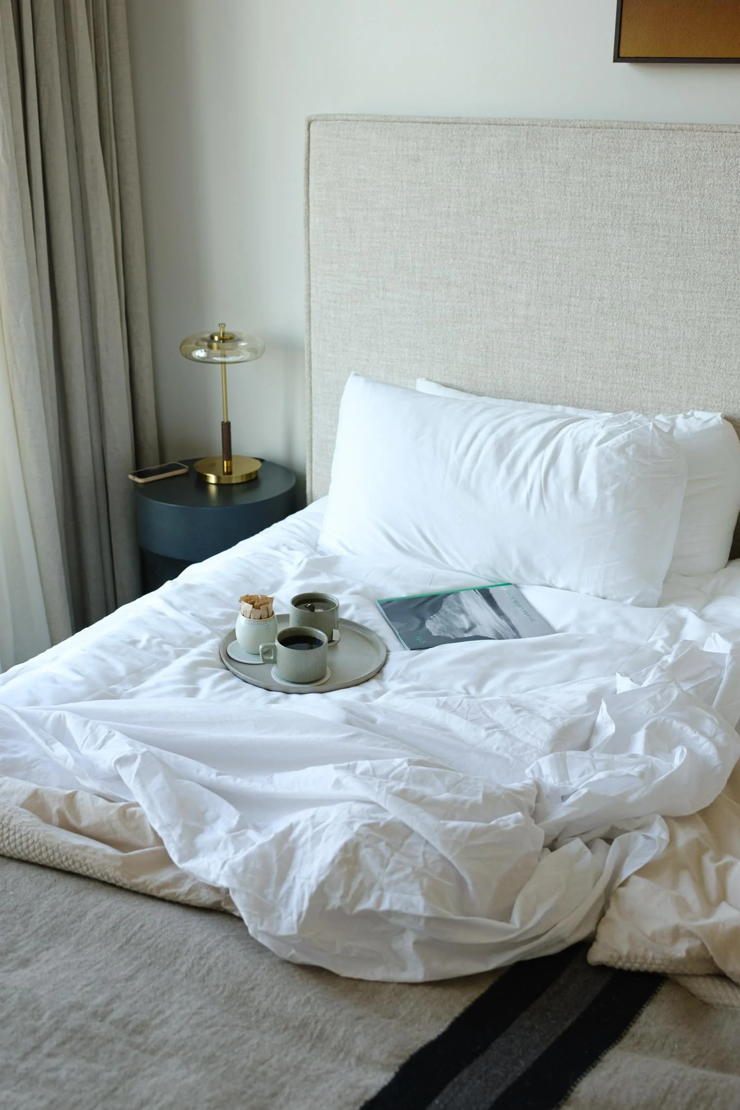 Guest bed with white bedding, coffee, and a surf book in a luxury guest room in Virginia Beach