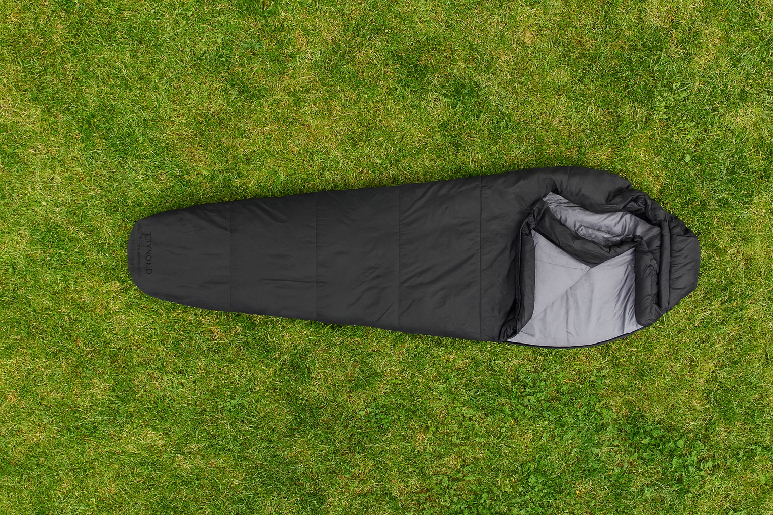 Sac de couchage noir étendu sur une pelouse verte