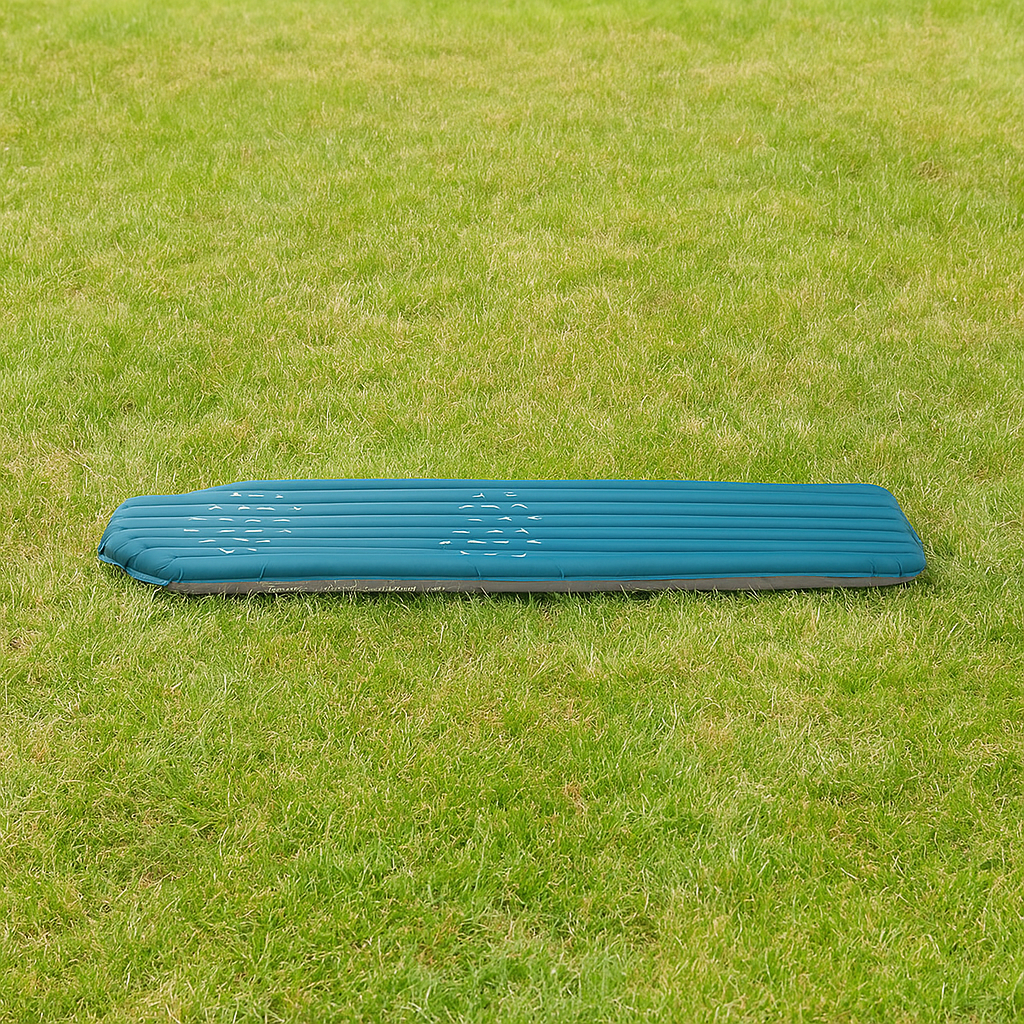 Matelas gonflable bleu posé sur l'herbe verte dans un espace extérieur.