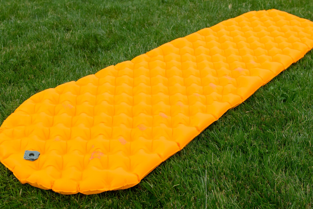 Un matelas de camping orange posé sur de l'herbe verte.