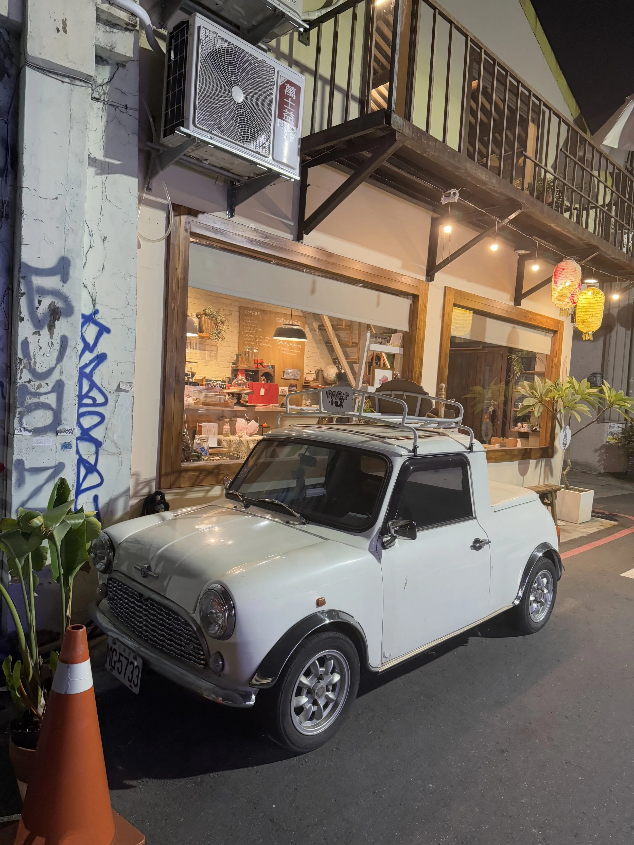 A vintage white Mini Cooper car parked outside a cafe at night in Tainan, Taiwan