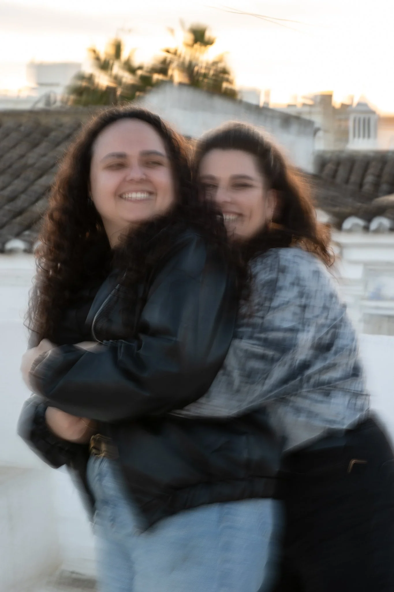 naispari, joista toinen halaa toista takaapäin, kuvassa näkyy liike-epäterävyys ja taustalla kattoja