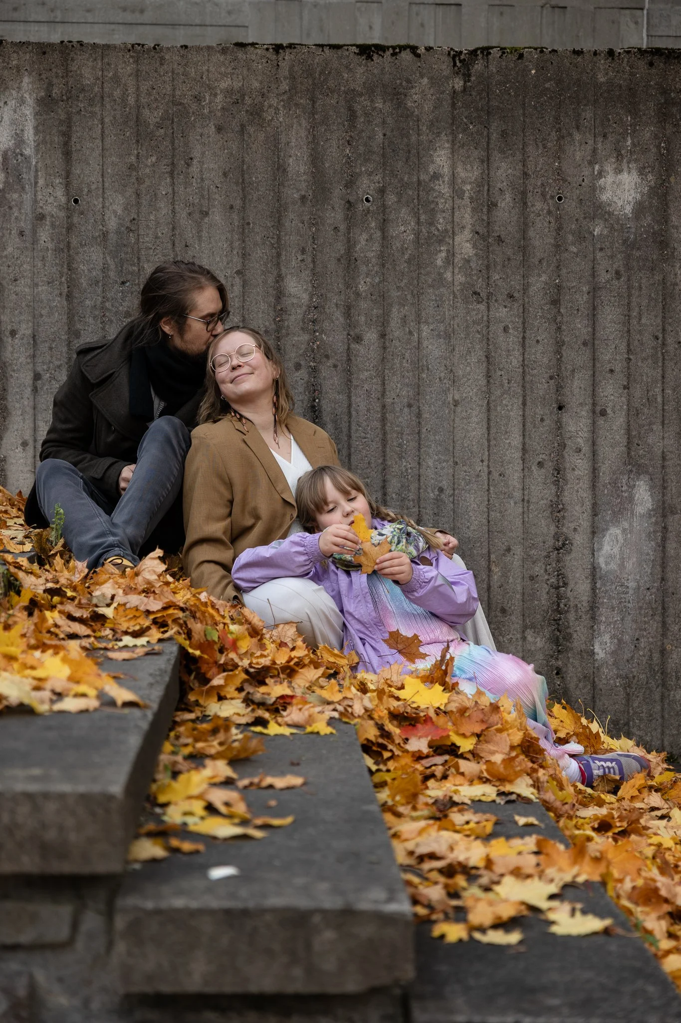 Perhe istuu portailla ja nojaa seinään, portaat täynnä keltaisia lehtiä