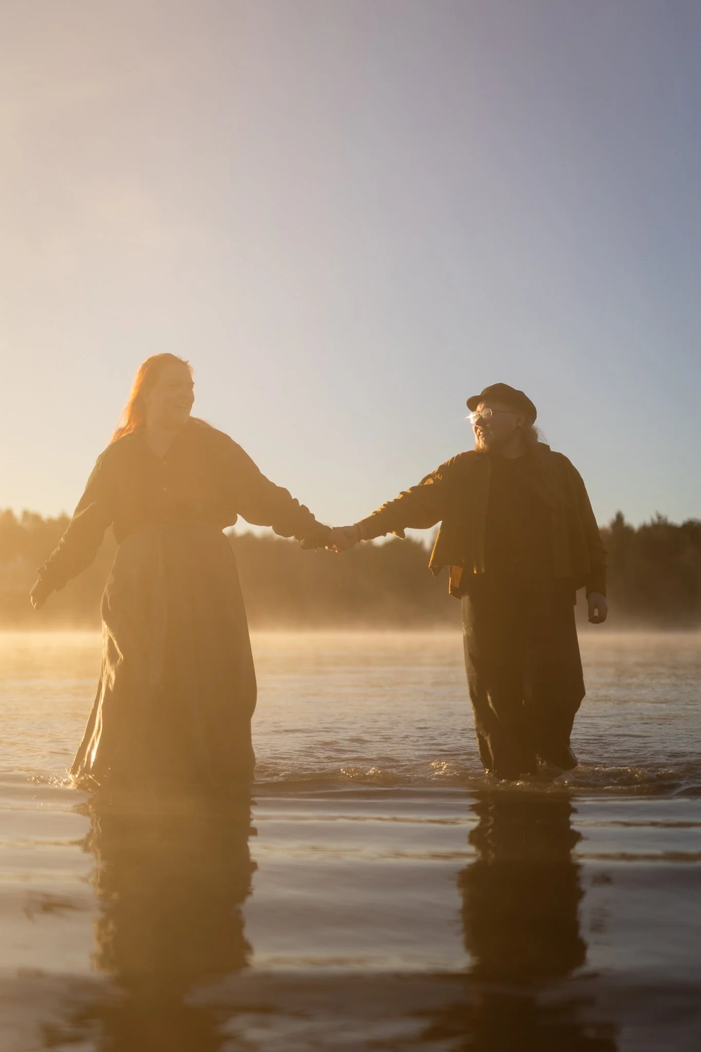 Pariskunta kahlaa meressä auringonnousussa, takana usvaa