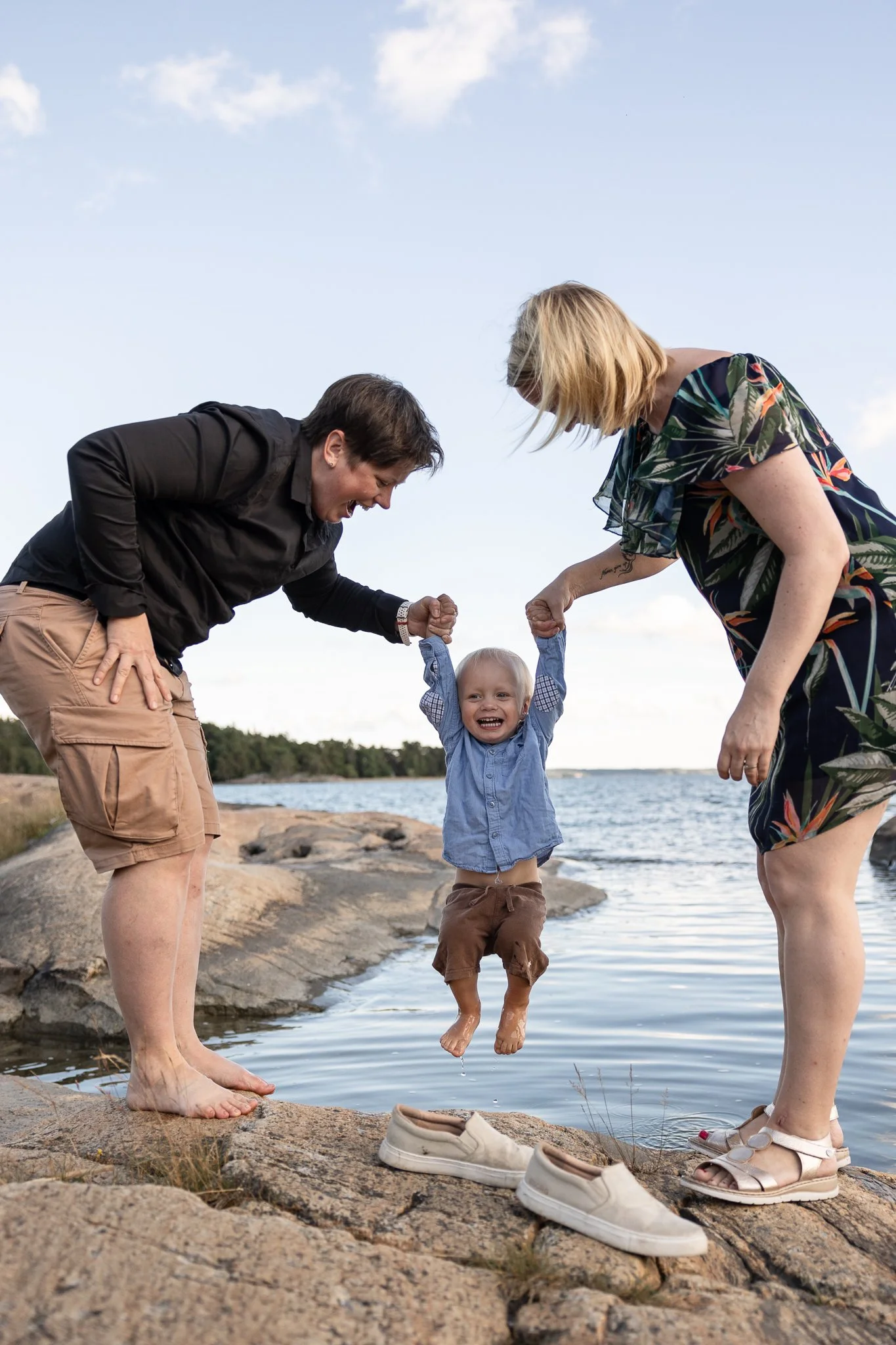Perhekuvaus Ruissalossa, kaksi äitiä pitää käsistä pientä lasta ja "dippaa" häntä veteen