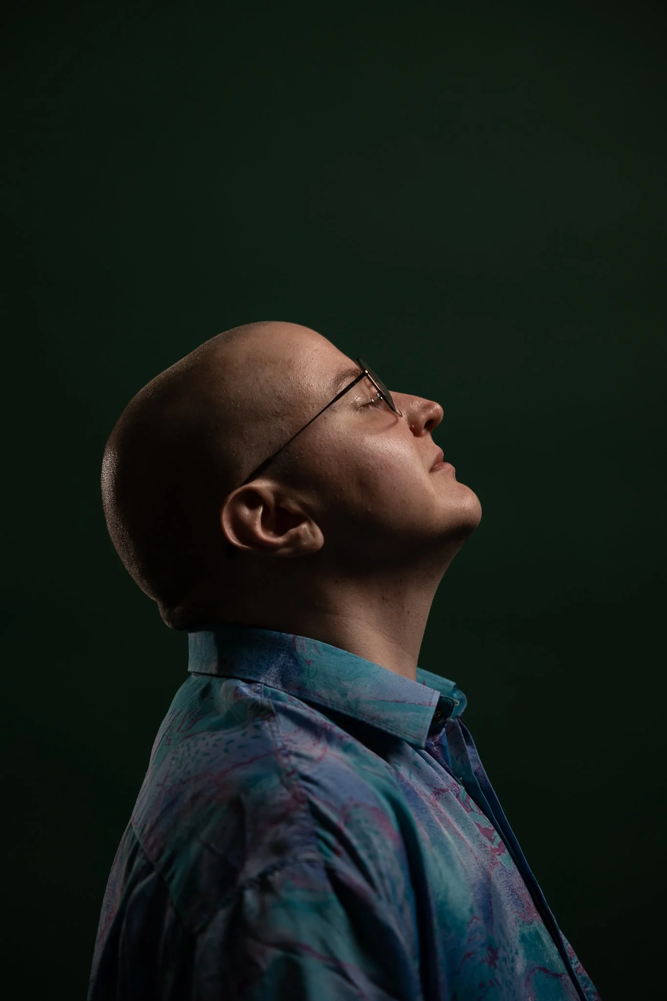 Kalju, valkoinen mies kuvattuna potrettirajauksella suoraan sivusta, hän kallistaa päätään taaksepäin silmät kiinni. Tausta on vihreä, päällään hänellä on sinisenkirjava kauluspaita ja silmälasit.