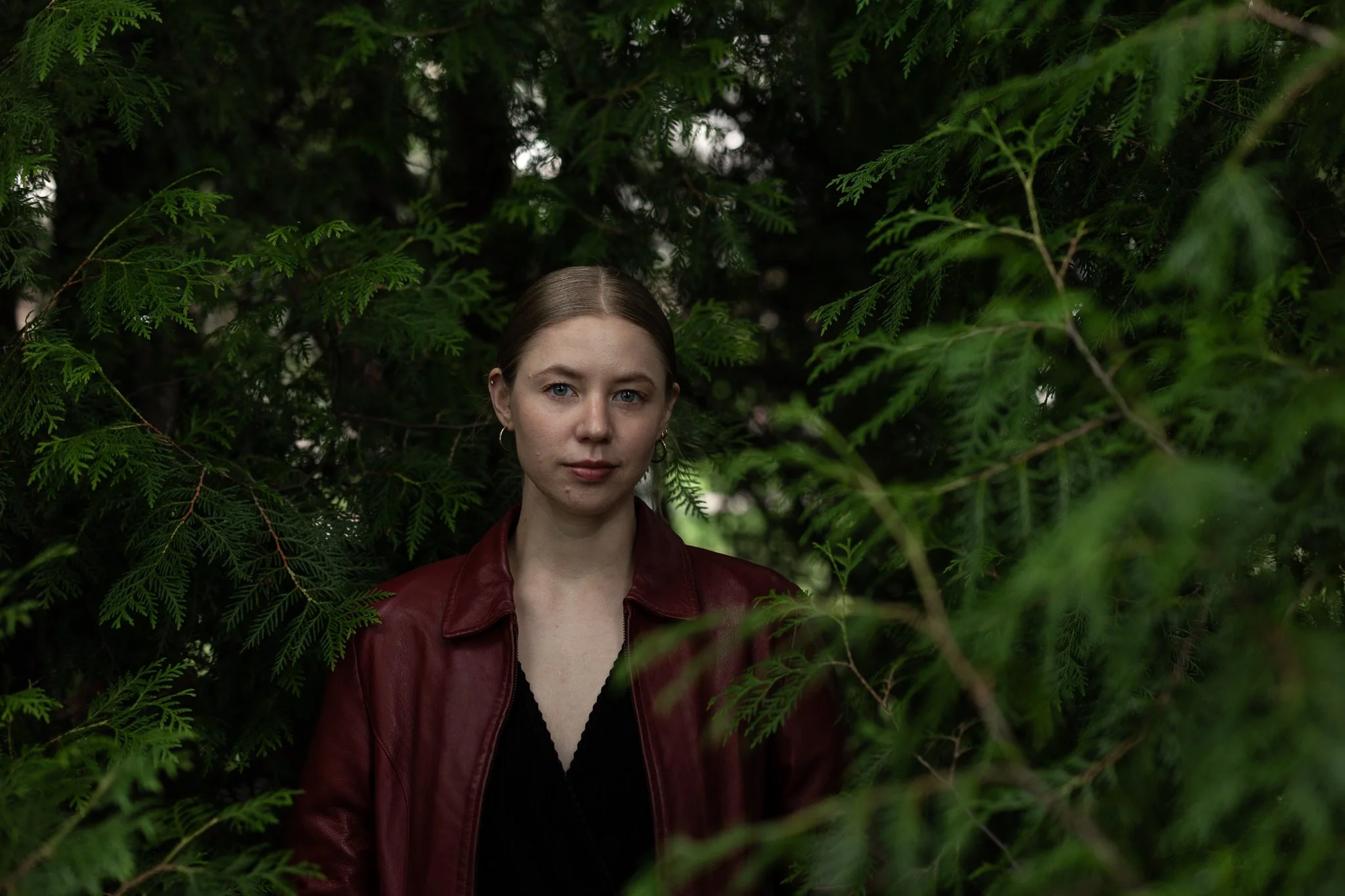 Henkilö on ikivihreän puun "sisällä", hän on keskellä kuvaa ja katsoo suoraan kameraan. Hänellä on siniset silmät, vaaleat hiukset ja valkoinen iho, päällään punainen nahkatakki, musta paita ja korvarenkaat. Kuva on puolikuva.