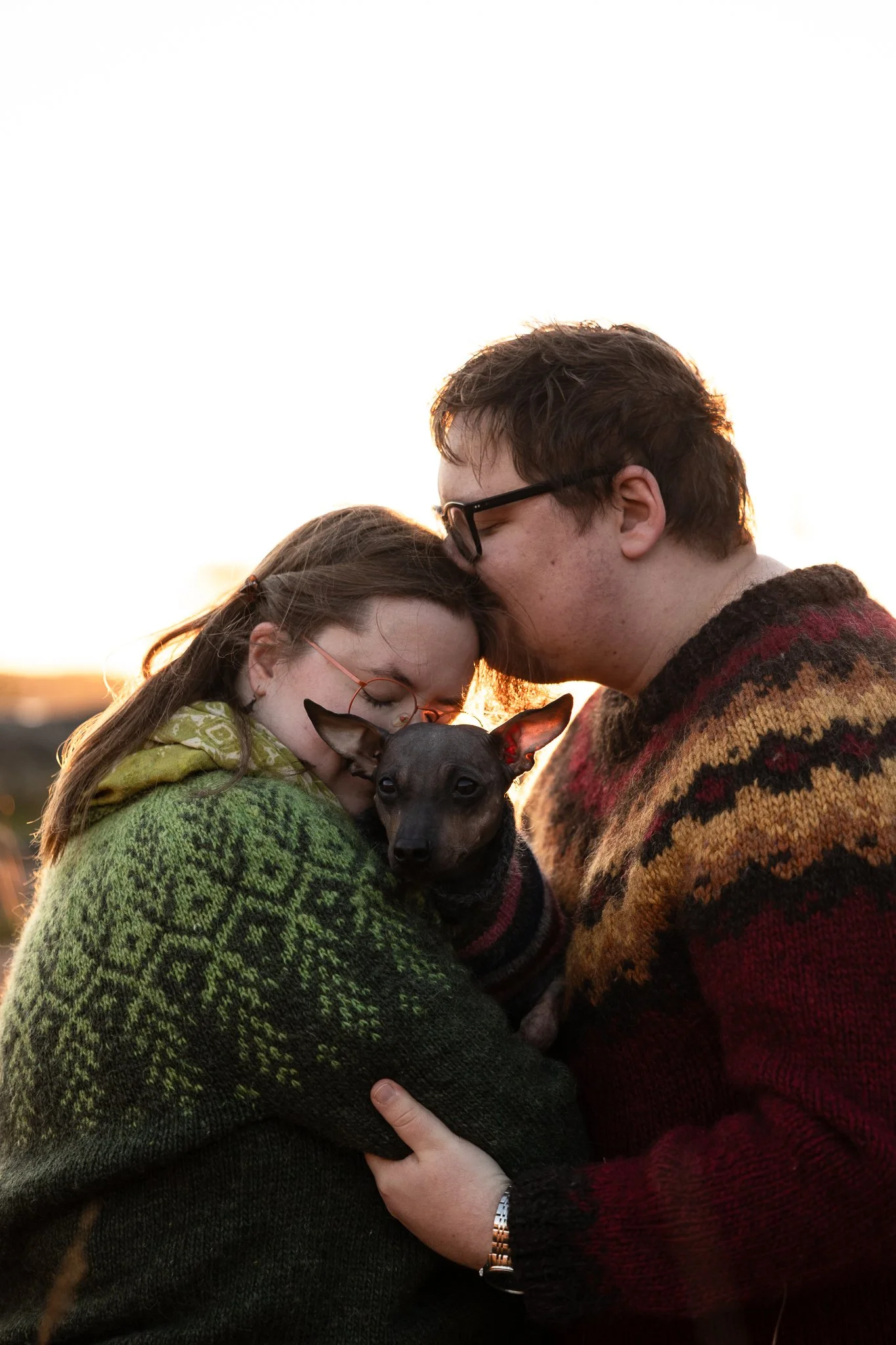 pariskunta seisoo kasvotusten, toisella on koira sylissä ja kasvot koiraa kohti, toisella on kasvot toisen hiuksissa