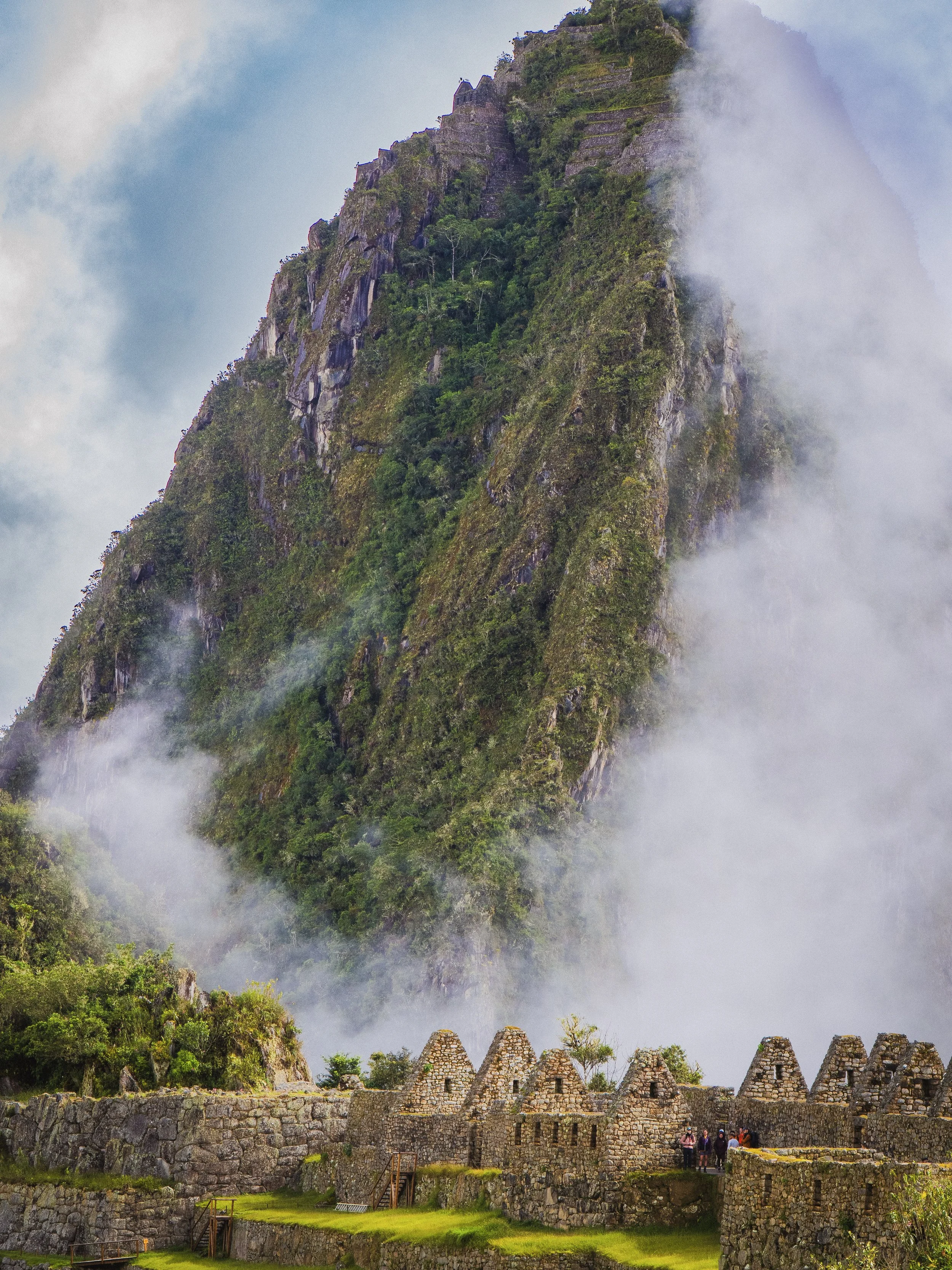 Ruines d'une ancienne ville inca en pierre devant une montagne couverte de végétation et partiellement enveloppée de brume ou de nuages. Machu Picchu
