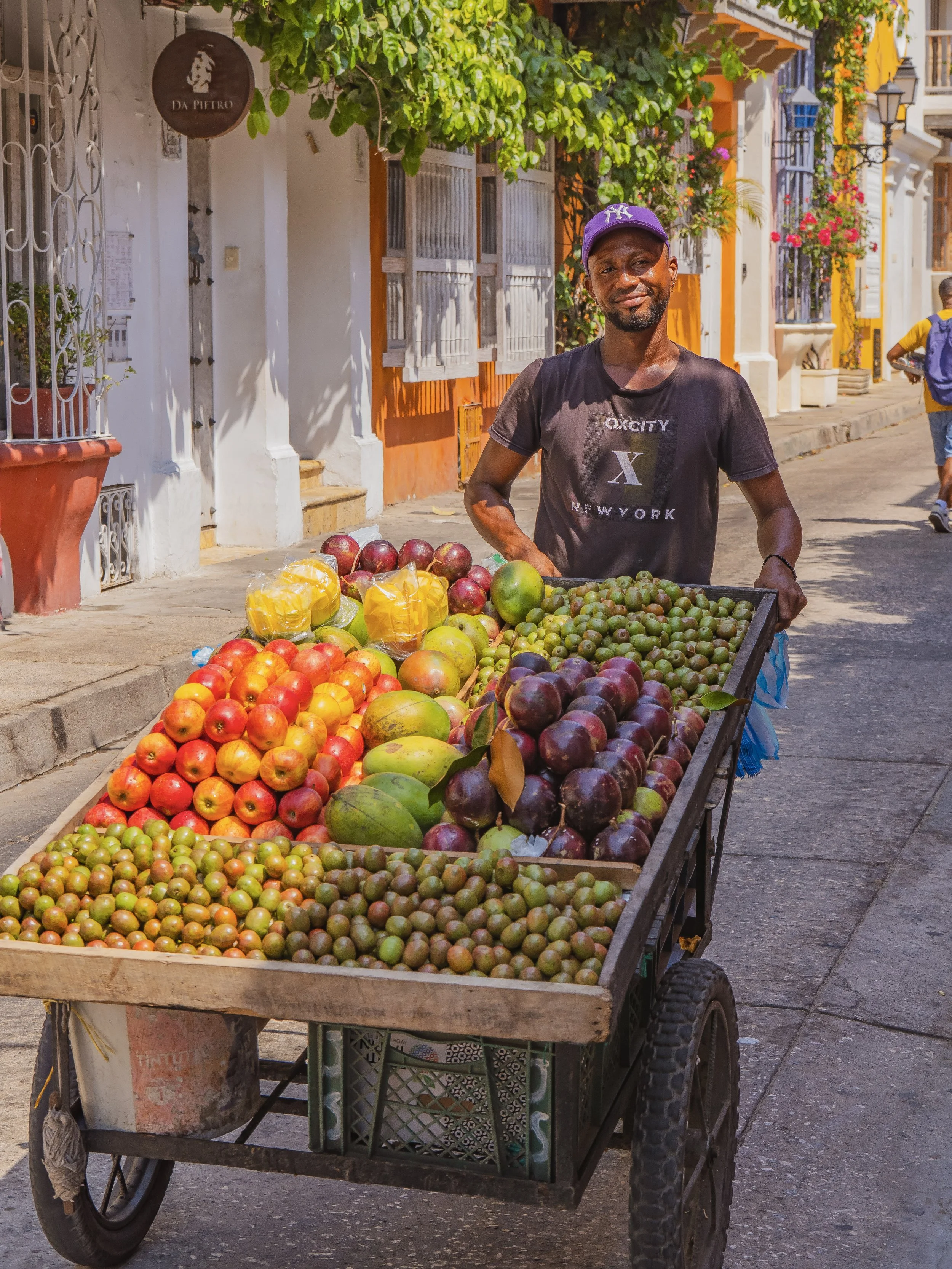Vendeur de fruits dans une rue colorée, entouré de maisons colorées et de fleurs
