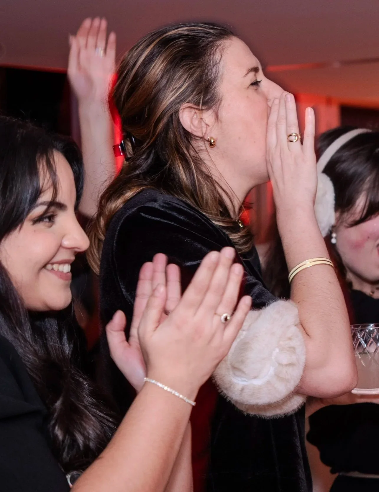Deux femmes applaudissent et semblent émues lors d'un événement, l'une d'elles couvre sa bouche avec la main