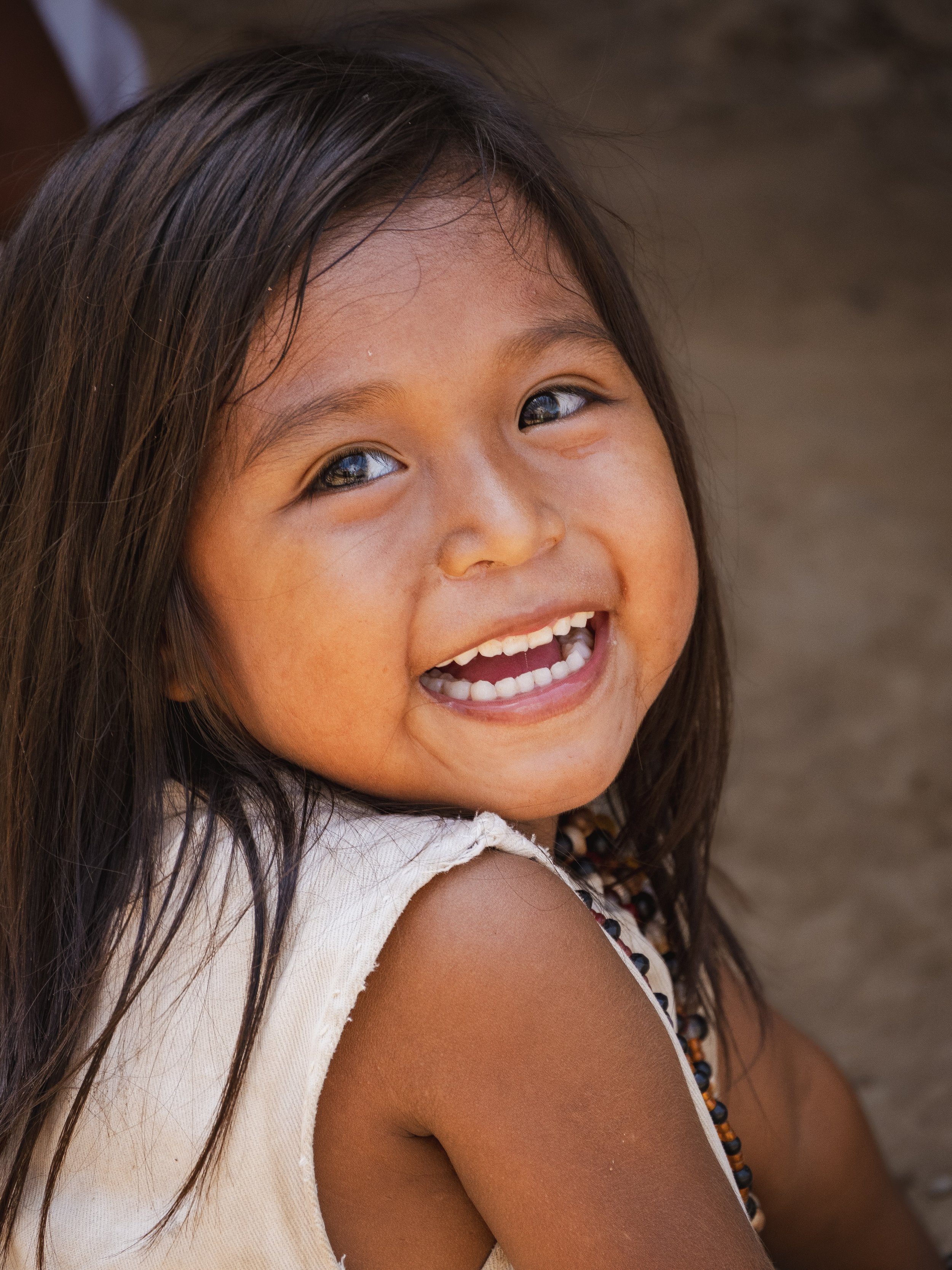 Une jeune fille souriante avec les cheveux longs et noirs, portant une tenue légère, dans un environnement naturel.