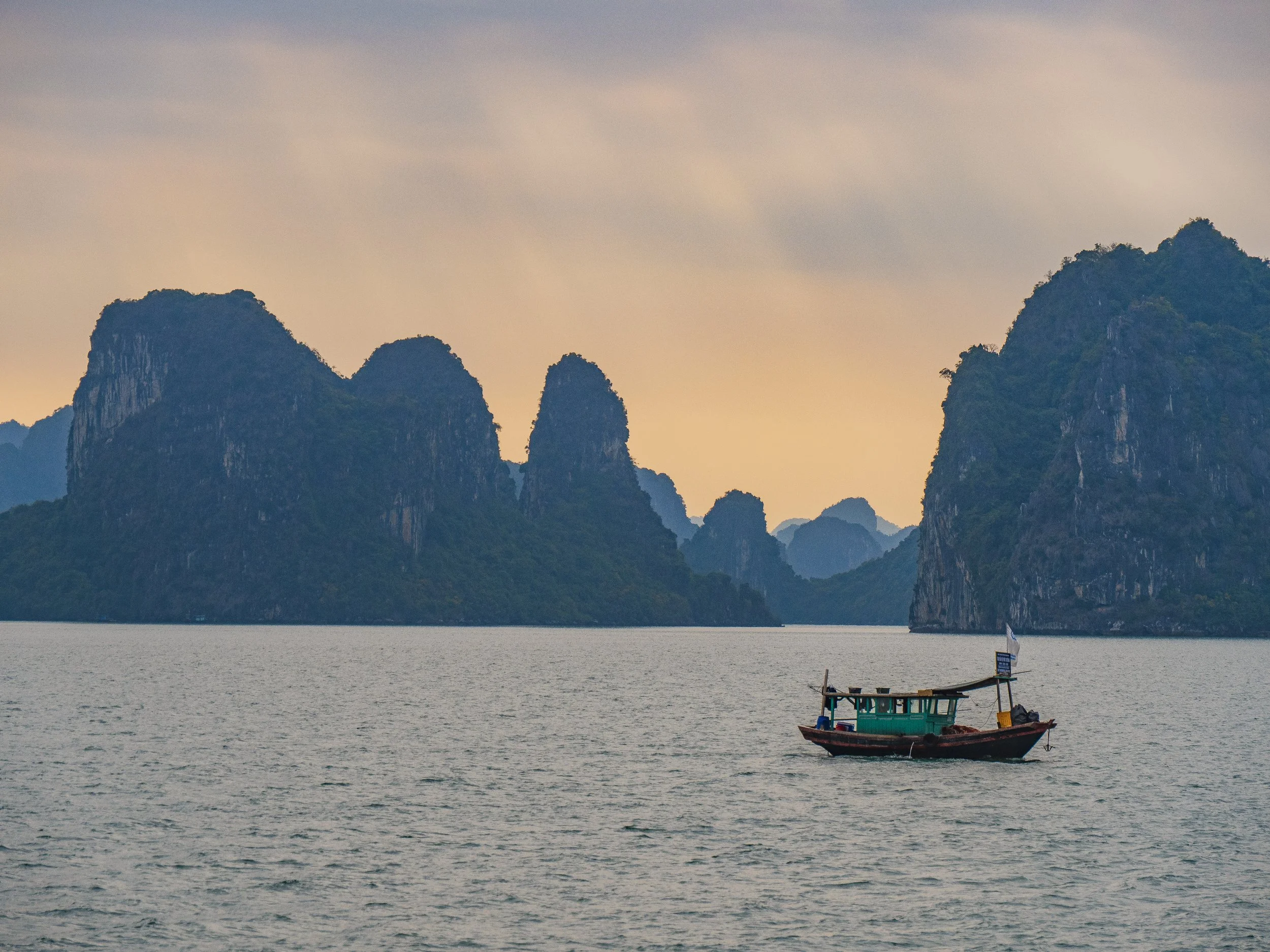 Un bateau navigate sur une mer calme avec des montagnes rocheuses en arrière-plan, sous un ciel nuageux.