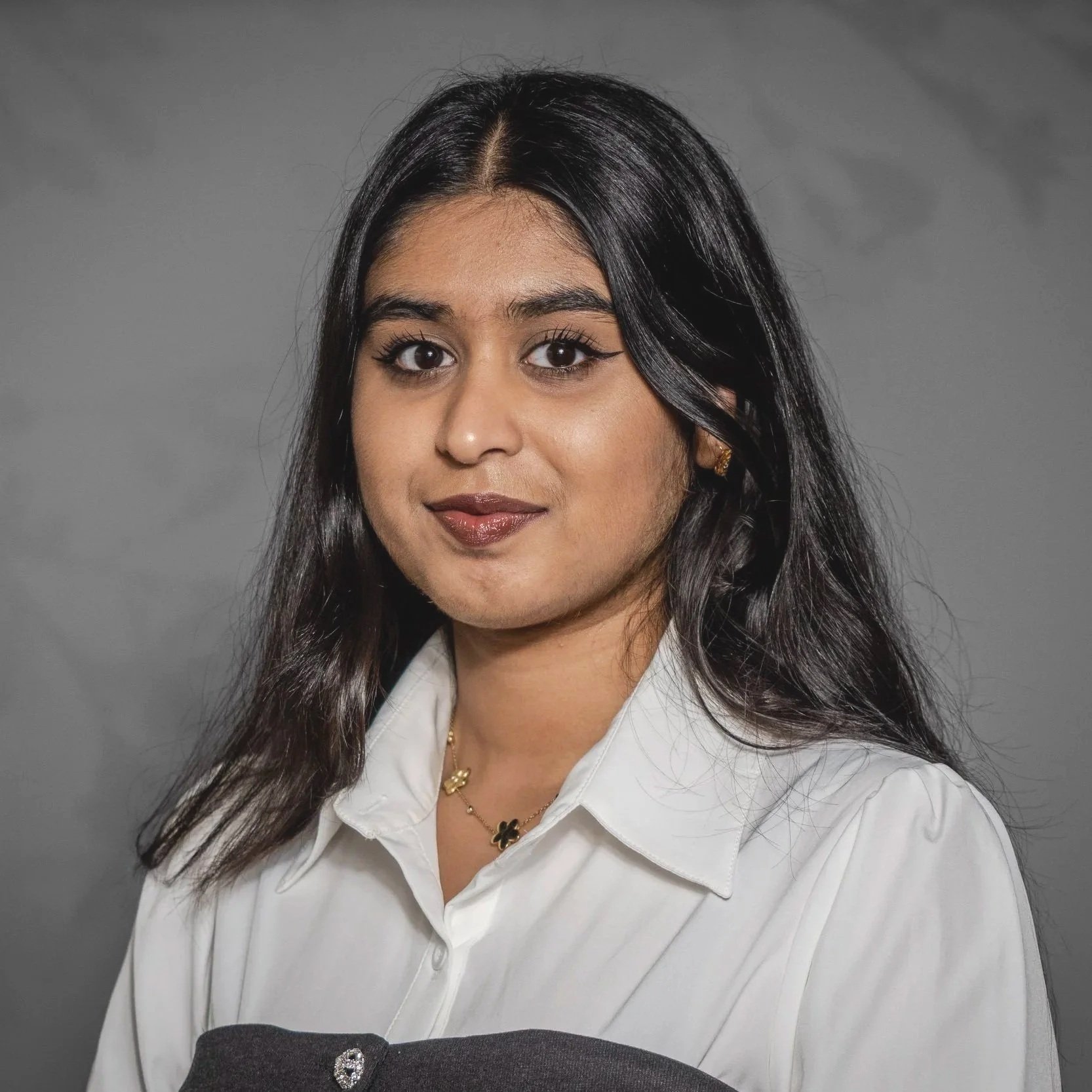 Portrait d'une femme avec des cheveux longs et noirs, portant une chemise blanche, un collier avec une fleur et un fond gris.