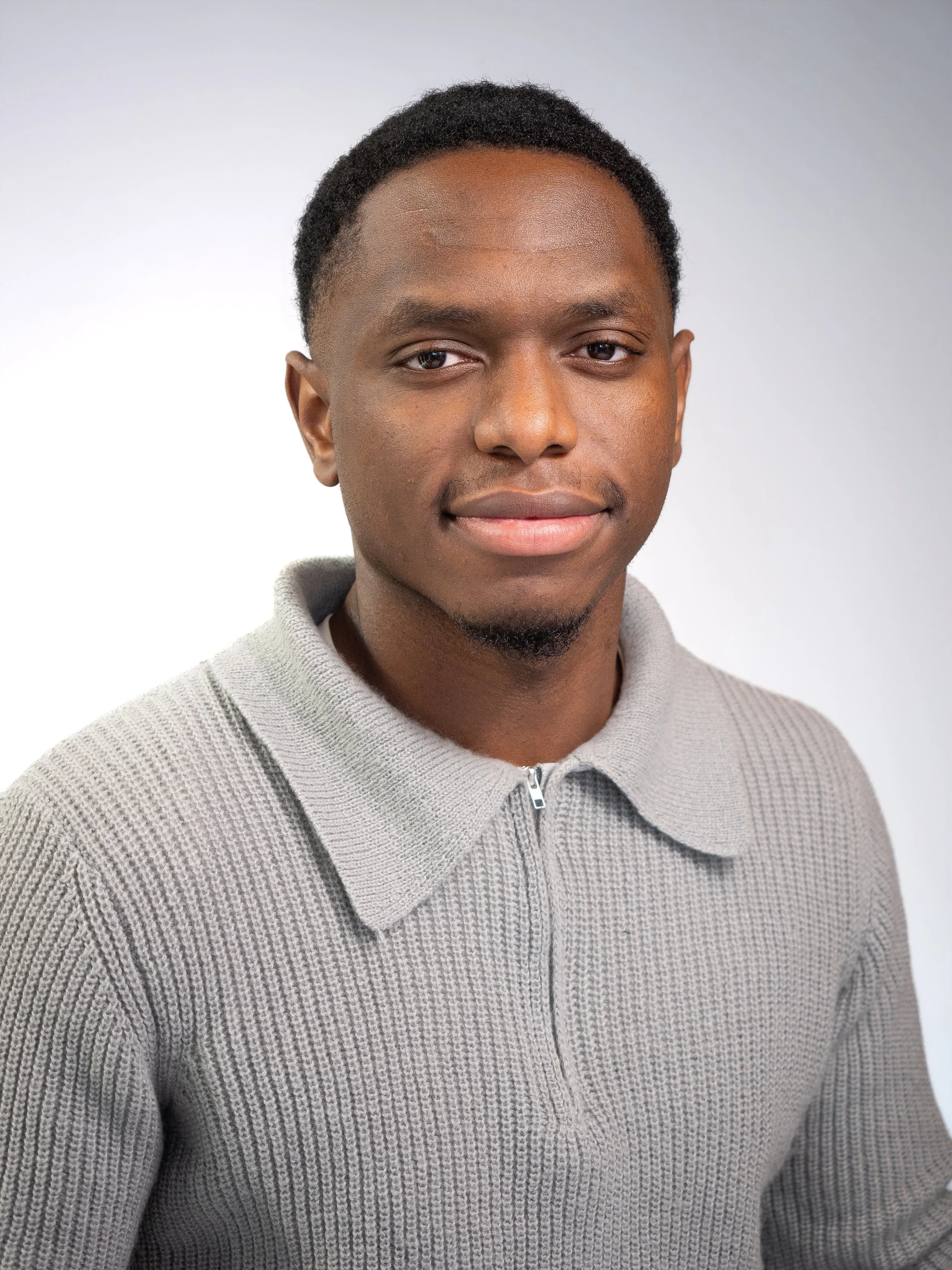 Portrait d'un jeune homme africain portant un pull gris avec un fond blanc.