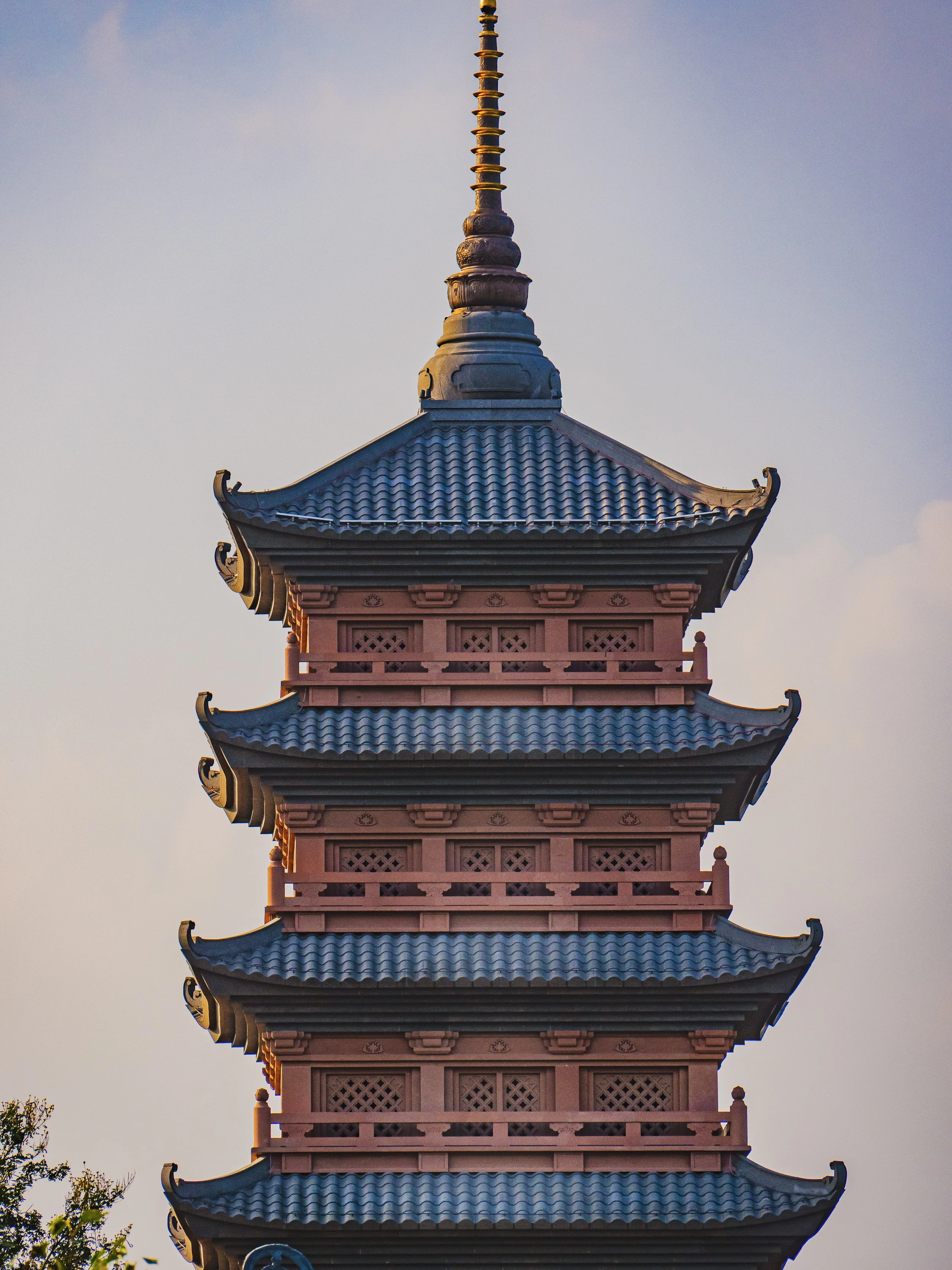 Une pagode à cinq étages avec des toits en tuiles bleues et des extrémités courbées, sous un ciel clair. Vietnam