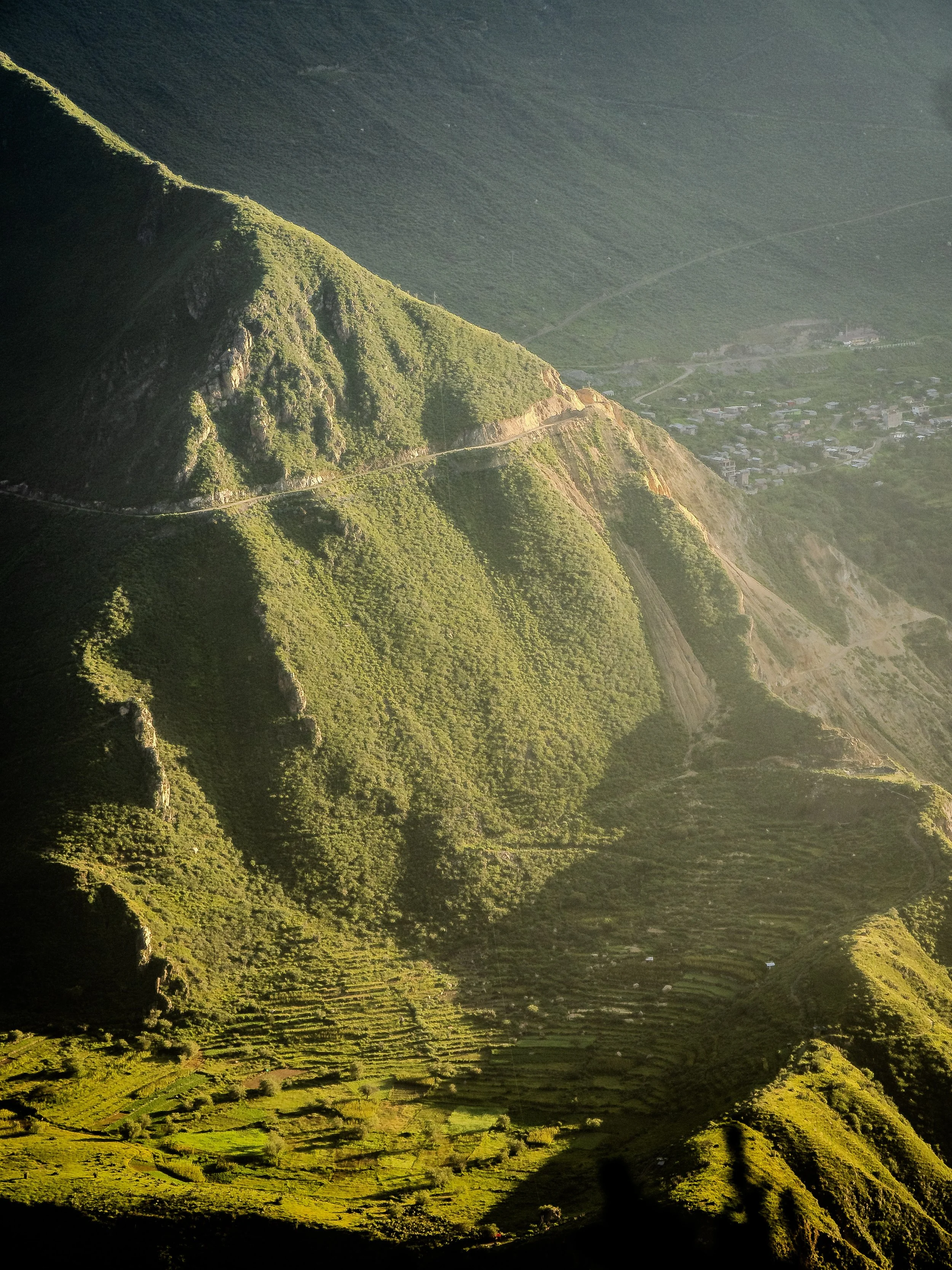 Paysage de montagnes verdoyantes avec terrasses agricoles en contrebas et un village au fond.