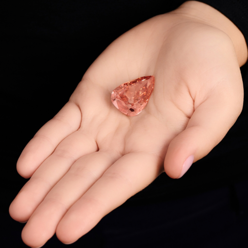 The Desert Rose, a 31.68 carat Fancy Vivid Orangy Pink pear shaped diamond, displayed on a hand to show its impressive size, vivid colour and exceptional brilliance.