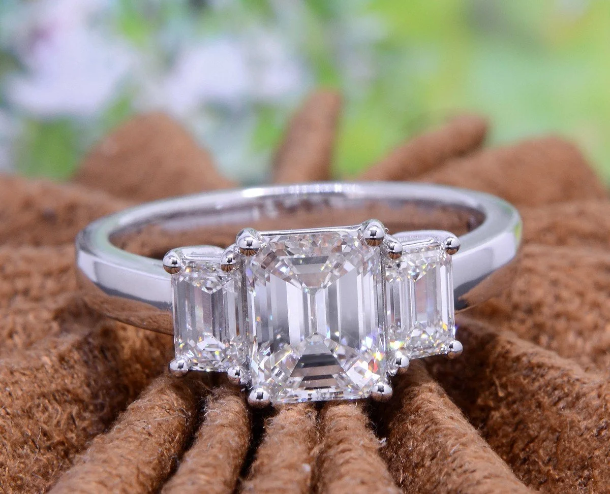 A three-stone engagement ring combining a round brilliant diamond with two tapered baguette side stones in 18kt white gold