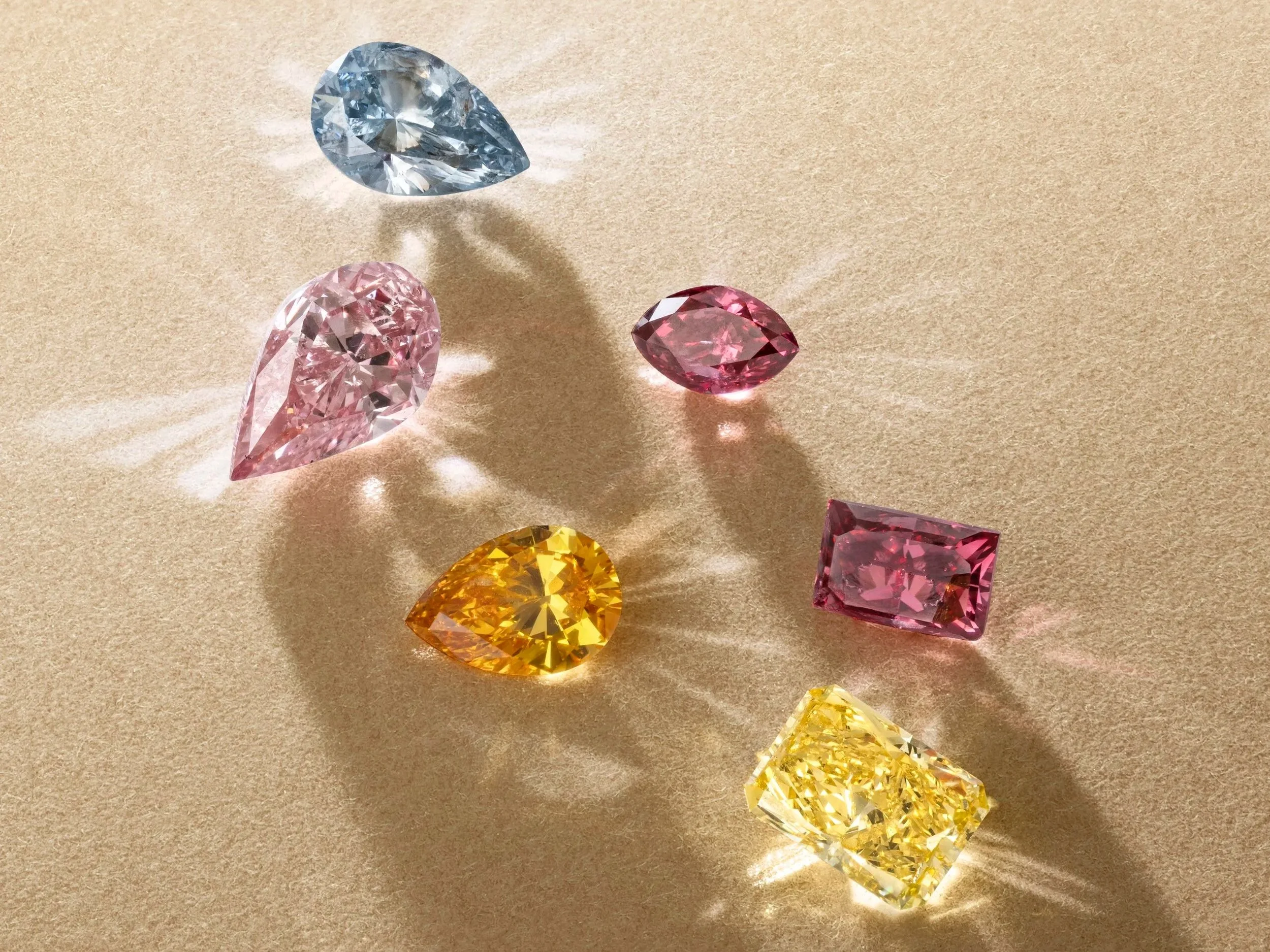 A curated array of over 300 loose fancy-coloured diamonds from The Rainbow Collection by Christie’s, showcasing hues from yellow and pink to blue and grey, photographed under soft lighting without background.