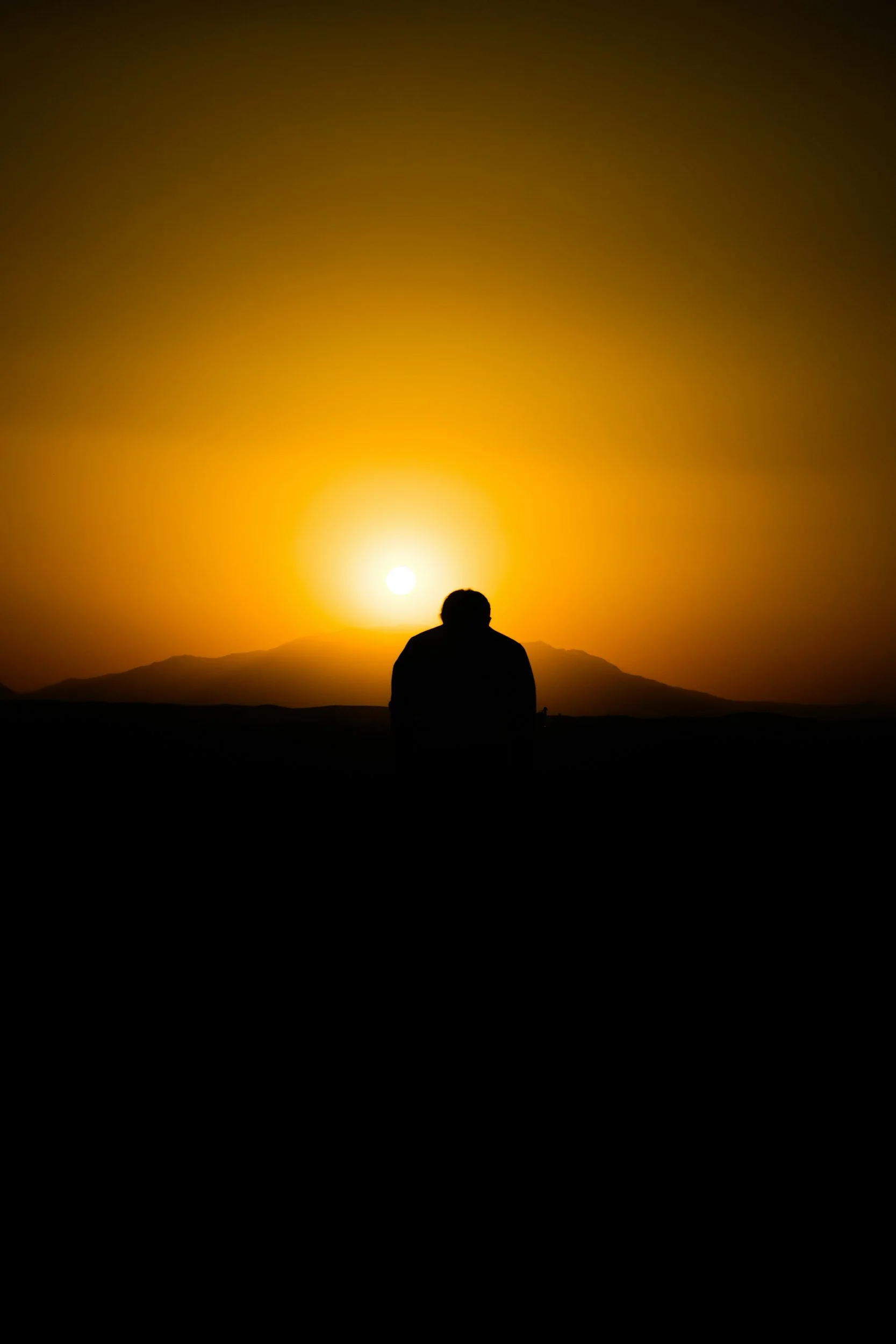 Silhuet af en person i en meditativ positur foran en gylden solnedgang over bjerge, der symboliserer indre ro og muligheden for at bygge et nyt fundament i livet.