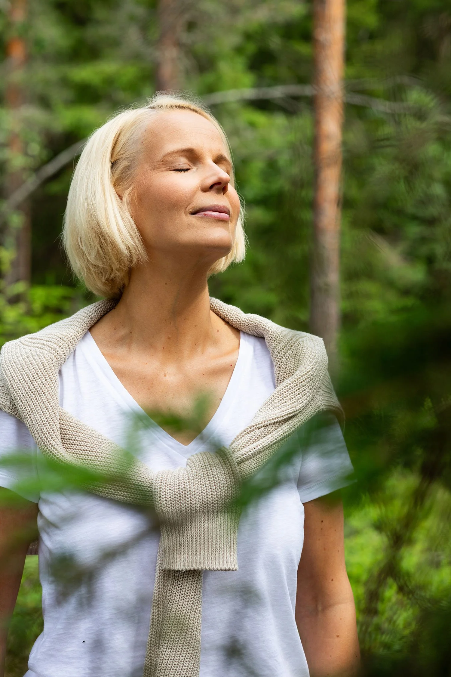 Nainen nauttii luonnosta metsässä, silmät kiinni, rennossa asennossa.