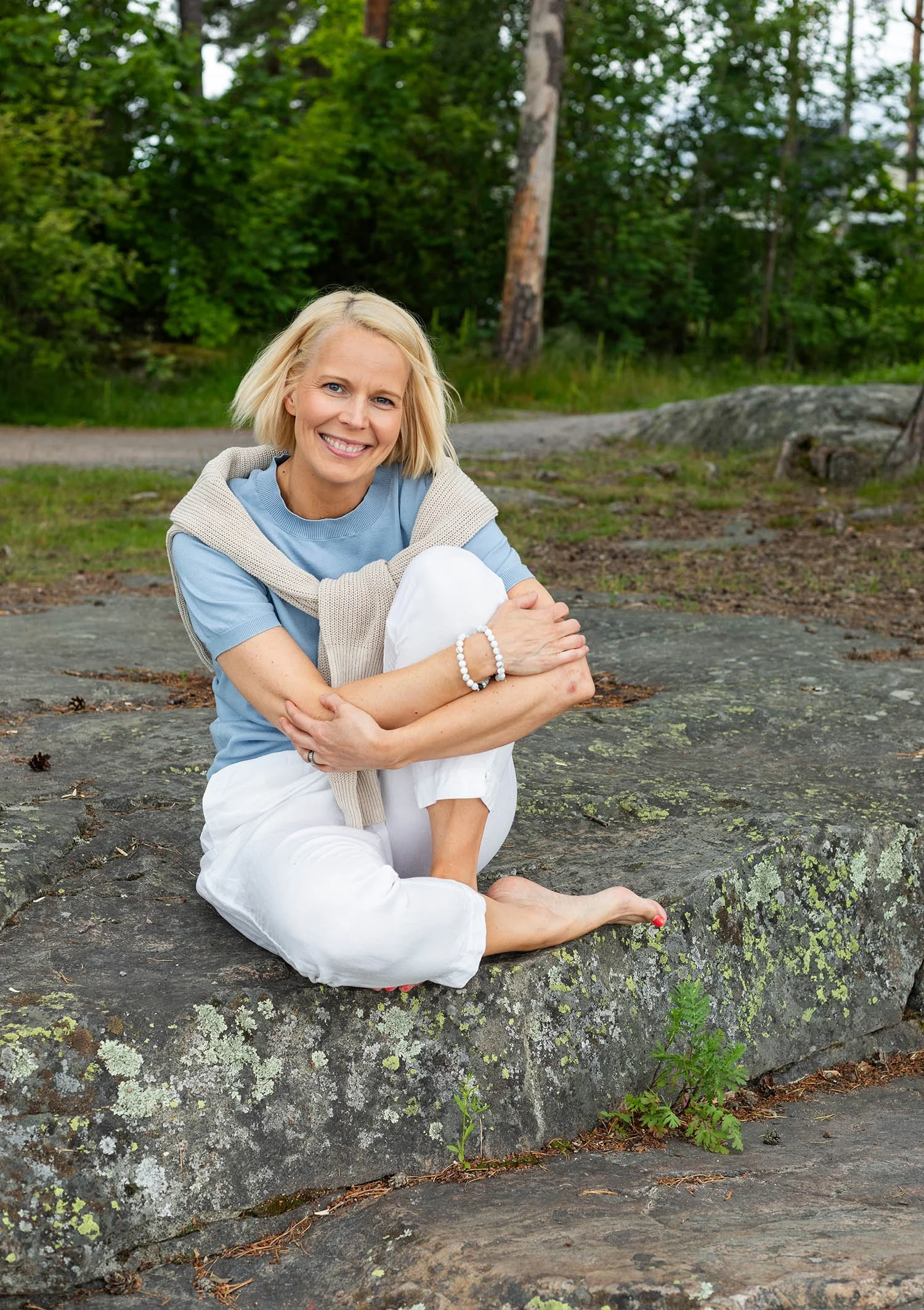 Susanna istuu kalliolla paljasjaloin ja hymyilee kameralle